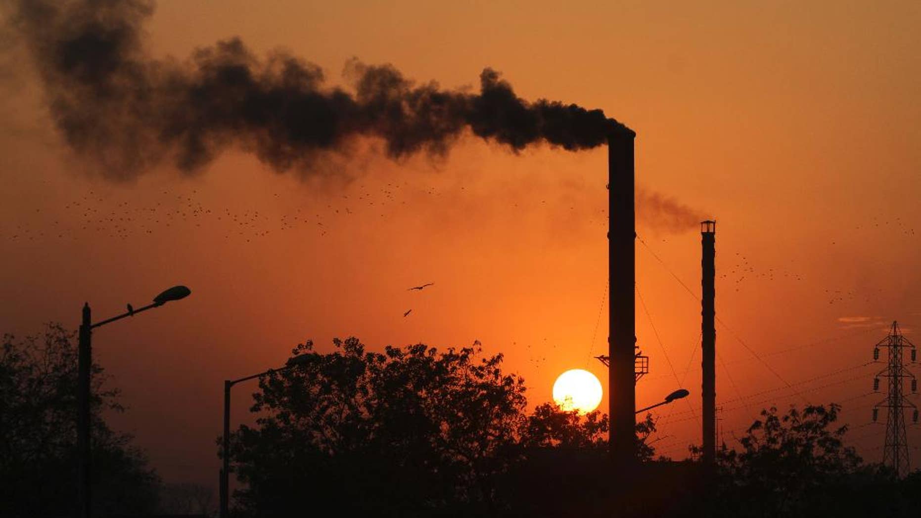 FILE - This is a Monday, Dec. 8, 2014 file photo of birds as they fly past at sun set as smoke emits from a chimney at a factory in Ahmadabad, India. The U.N.'s scientific panel on climate change will write a special report on how to limit global warming to 1.5 degrees Celsius (2.7 degrees Fahrenheit) compared with pre-industrial times. Temperatures have already risen almost 1 degree C (1.8 F) since humans started burning fossil fuels — the biggest source of greenhouse gases — on an industrial scale in the 19th century. (AP Photo/Ajit Solanki, File)