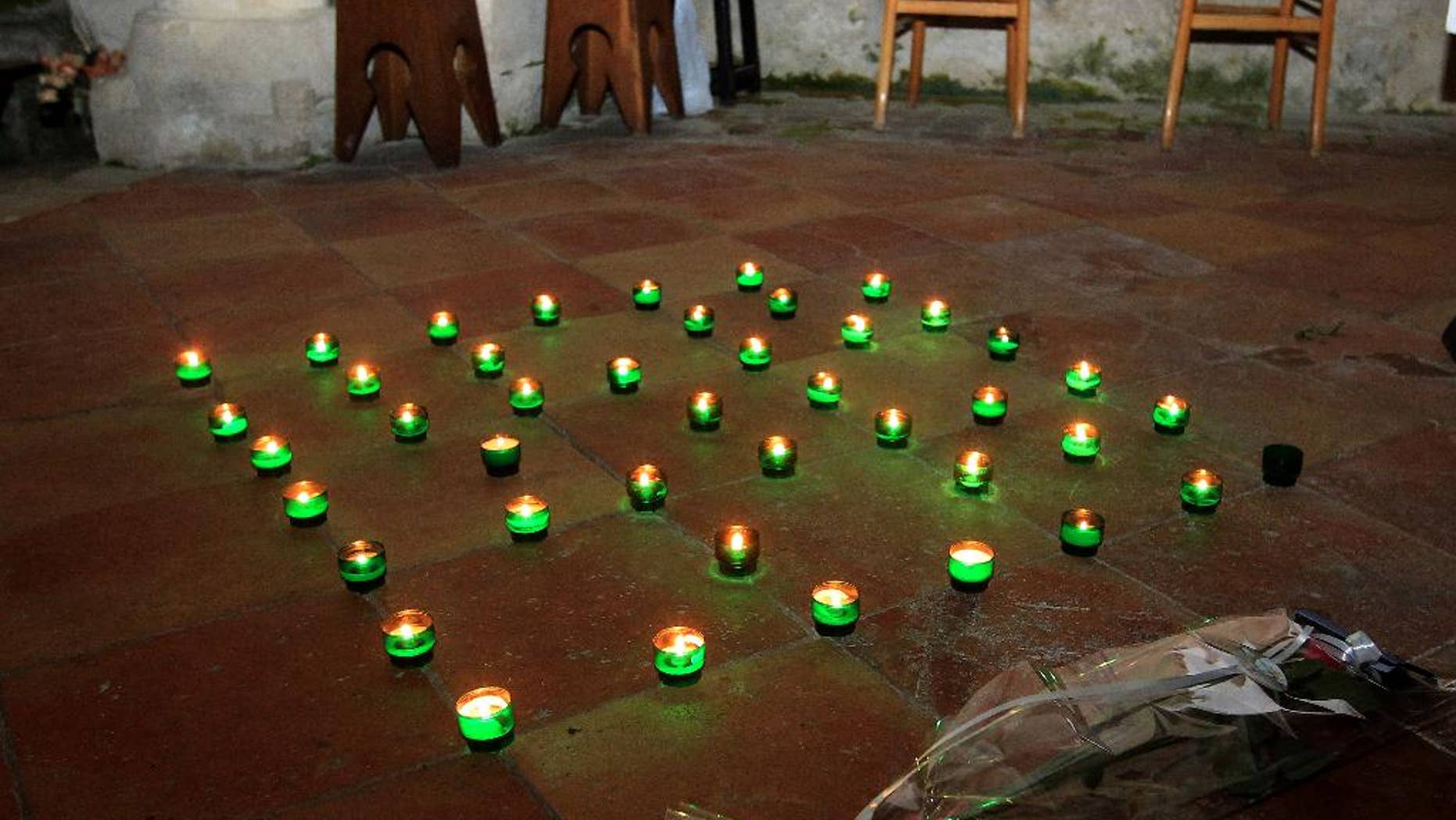 Candles and a bunch of flowers are placed on the ground inside a church in Petit-Palais-et-Cornemps, near the crash site of Puisseguin, southwestern France, in memory of the 43 victims of a road crash, Friday, Oct. 23, 2015. A truck and a bus transporting retirees on a day trip collided and caught fire Friday on a country road in wine country in southwest France, killing 43 people and gravely injuring at least four others, authorities said. (AP Photo/Bob Edme)