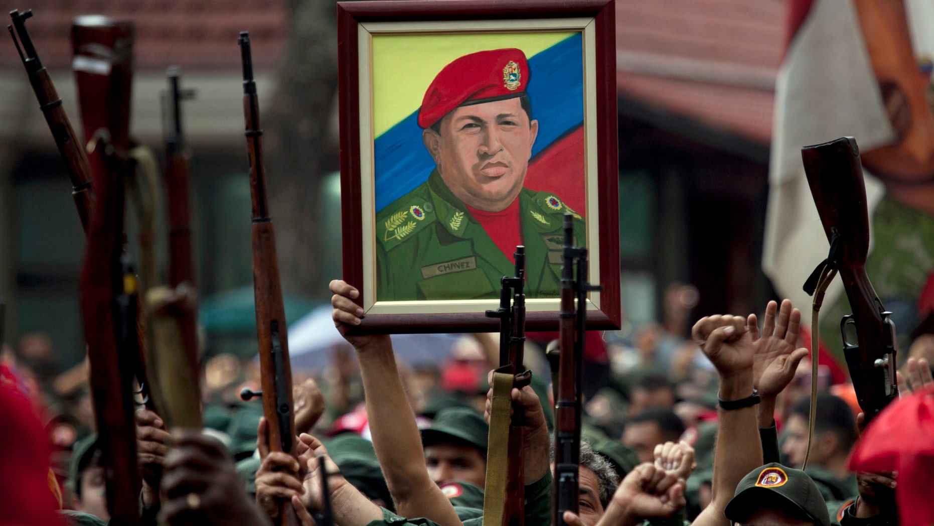 In this April 13, 2010 file photo, members of the National Revolutionary Militia hold up their weapons and a painting of Venezuela's President Hugo Chavez at an event marking the 9th anniversary of Chavez's return to power after a failed 2002 coup, in Caracas, Venezuela. (AP Photo/Ariana Cubillos, File)