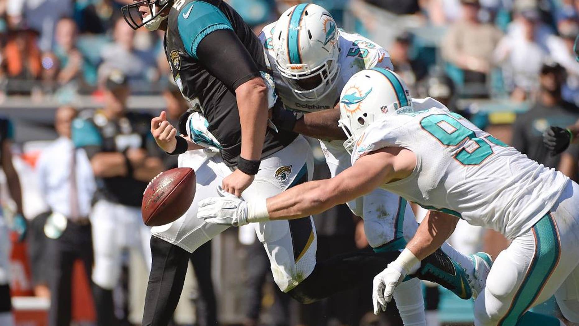 Jacksonville Jaguars quarterback Blake Bortles, left, fumbles the ball as he is hit by Miami Dolphins middle linebacker Jason Trusnik, right, and linebacker John Lotulelei, center, during the first half of an NFL football game in Jacksonville, Fla., Sunday, Oct. 26, 2014. (AP Photo/Phelan M. Ebenhack)