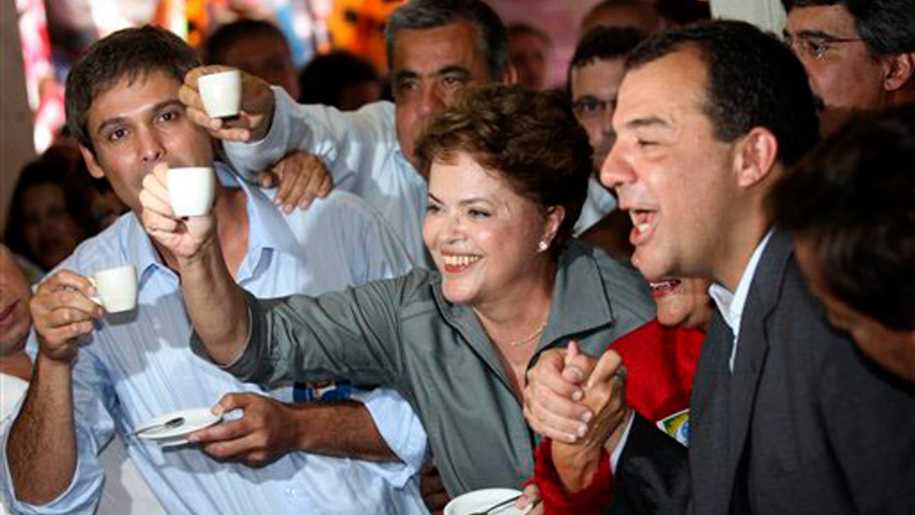 Brazil's Workers party presidential candidate Dilma Rousseff, center, holds up a cup of coffee at a coffee shop during a campaign rally in Rio de Janeiro, Brazil, Monday, Sept. 20, 2010.