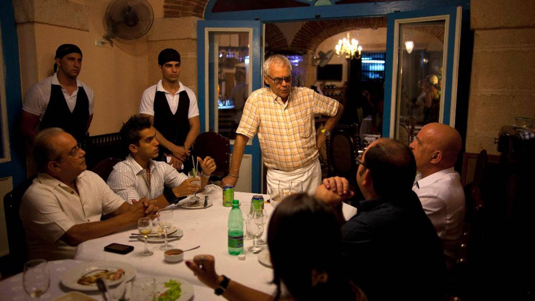 FILE - In this July 11, 2012 file photo, Tomas Erasmo Hernandez, center, owner of the private restaurant Mama Ines, chats with his customers in Old Havana, Cuba. Cuba is temporarily freezing new licenses for private restaurants in Havana, announced by acting Vice President Isabel Hamze on state media on Wednesday, Oct. 19, 2016. The city is also starting to impose more limits on private bed-and-breakfasts. (AP Photo/Ramon Espinosa, File)