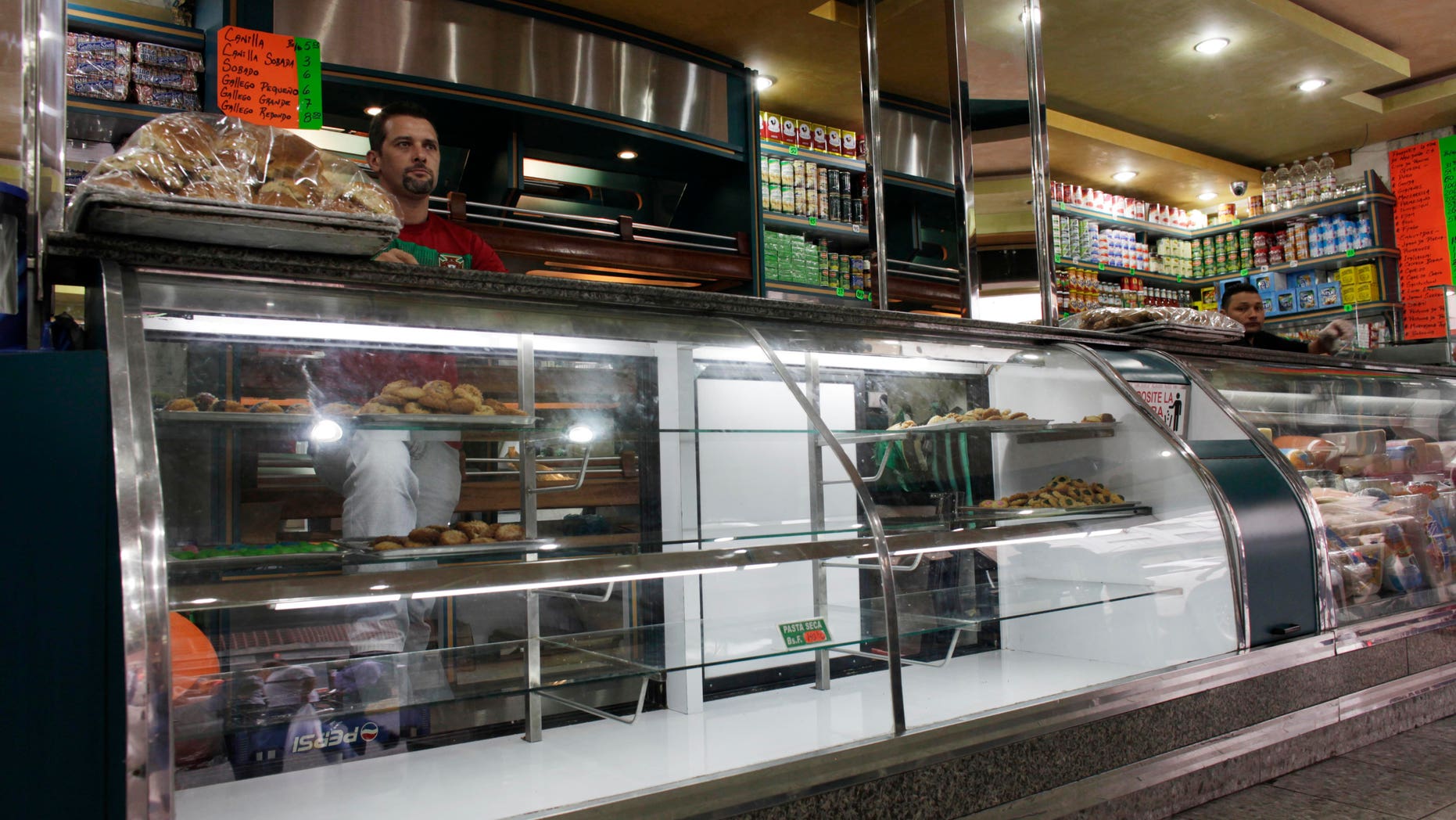 A bakery worker stand behind of a nearly empty display case in Caracas, Venezuela, Wednesday, Jan. 30, 2013. Venezuelans have been coping with sporadic shortages of foods ranging from cooking oil to sugar, and lately a dearth of flour is preventing some bakeries from making bread. (AP Photo/Ariana Cubillos)