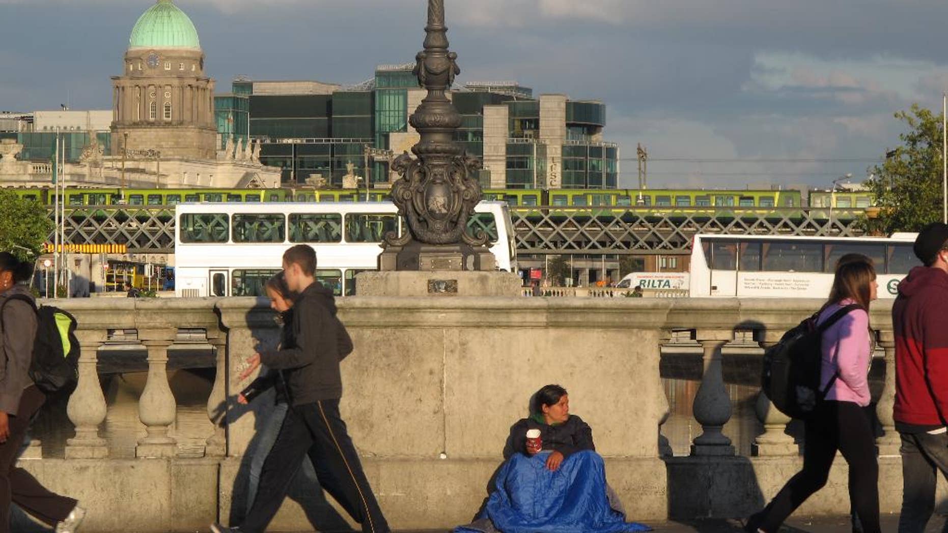 In this picture taken on Monday, Oct. 6, 2014, pedestrians pass a street beggar on O'Connell Bridge in central Dublin, Ireland, with the city's financial district in the background. Ireland is rebounding strongly from its 2010 international bailout and seeking to repay its International Monetary Fund loans early to save on interest costs. (AP Photo/Shawn Pogatchnik)