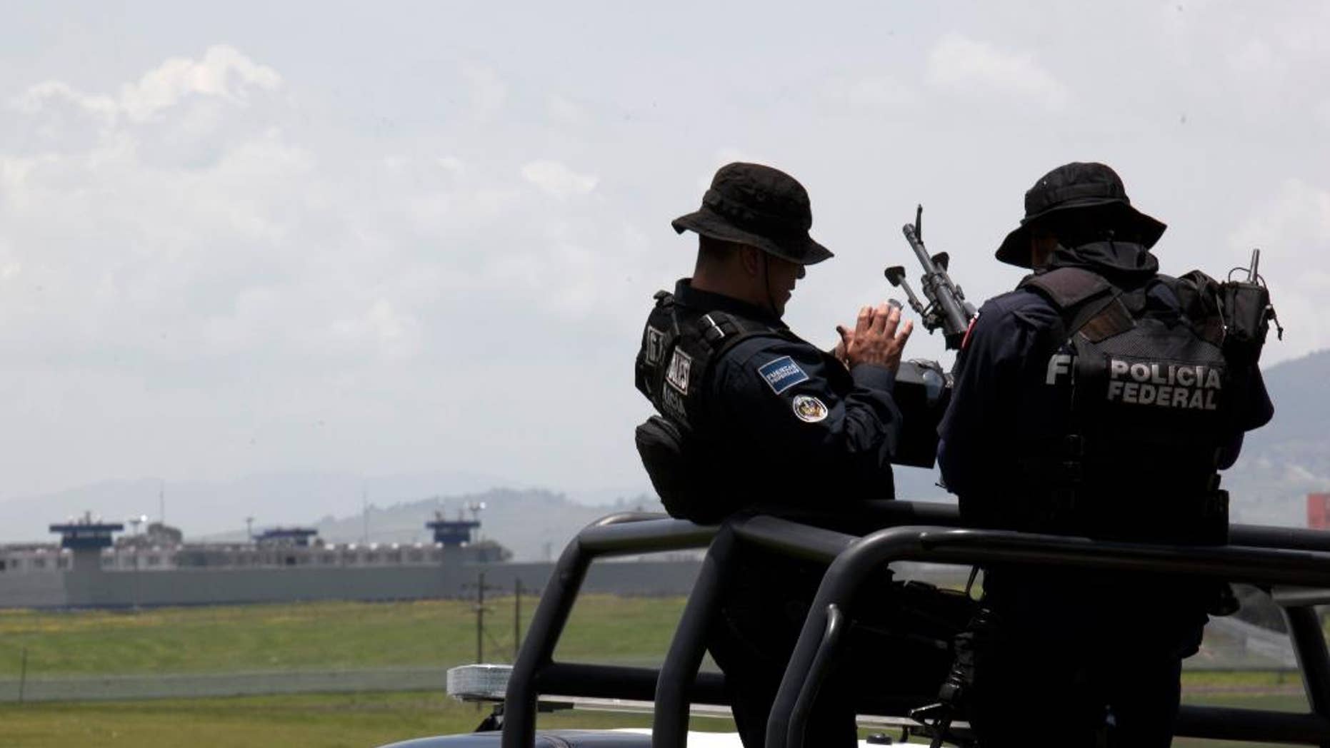 Federal Police man their weapons aboard a pick up truck, near the half-built house where drug lord Joaquin "El Chapo" Guzman made his escape through a tunnel from the Altiplano maximum security prison in Almoloya, west of Mexico City, Monday, July 13, 2015. The Altiplano prison can be seen in the background. A widespread manhunt that included highway checkpoints, stepped up border security and closure of an international airport failed to turn up any trace of "El Chapo" Guzman by Monday, more than 24 hours after he escaped through an underground tunnel in his cell. (AP Photo/Marco Ugarte)