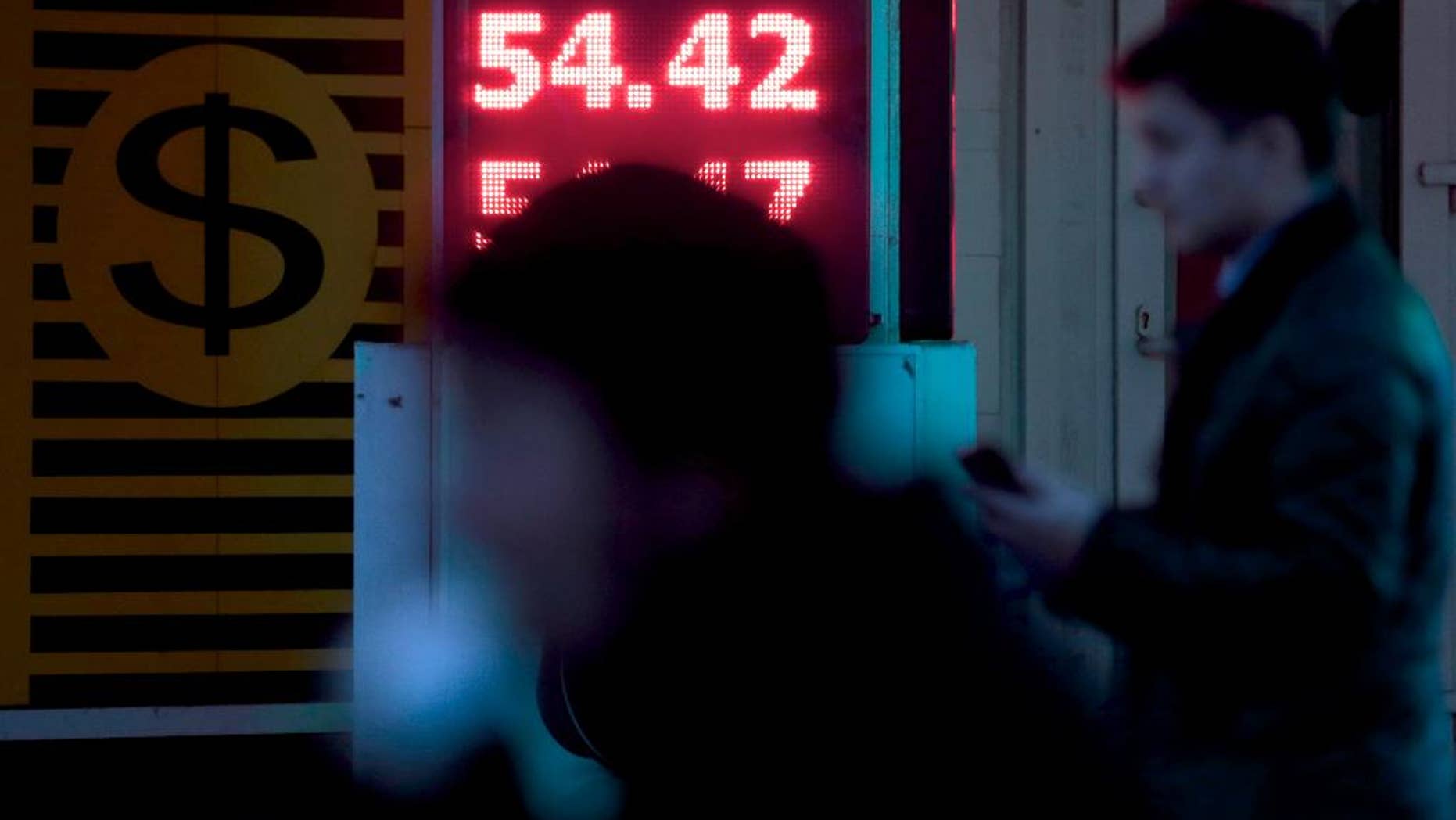 FILE - In this Tuesday, Oct. 28, 2014, photo from files people pass by an exchange rate display at a street in Moscow, Russia, showing an exchange rate of 54.42 for the ruble against the euro. The central bank announced on Wednesday, Nov. 5, 2014 that it will limit the daily volume of foreign exchange operations to 350 million dollars in order to stabilize the ruble. (AP Photo/Ivan Sekretarev, File)