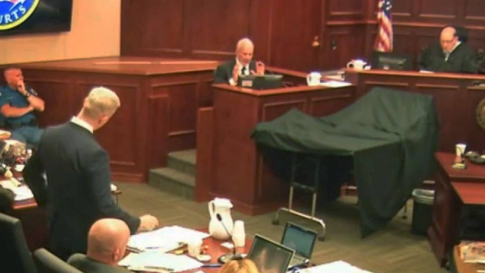 District Attorney George Brauchcer, left, questions state-appointed psychiatrist Dr. Jeffrey Metzner, center, as Judge Carlos Samour, Jr., looks on at right during trial testimony in Centennial, Colo., Monday, June 8, 2015. Metzner testified that Colorado theater shooter James Holmes was mentally ill at the time of a deadly attack that killed 12 people and wounded 70 others during the midnight premiere of a Batman film. (Colorado Judicial Department via AP, Pool)