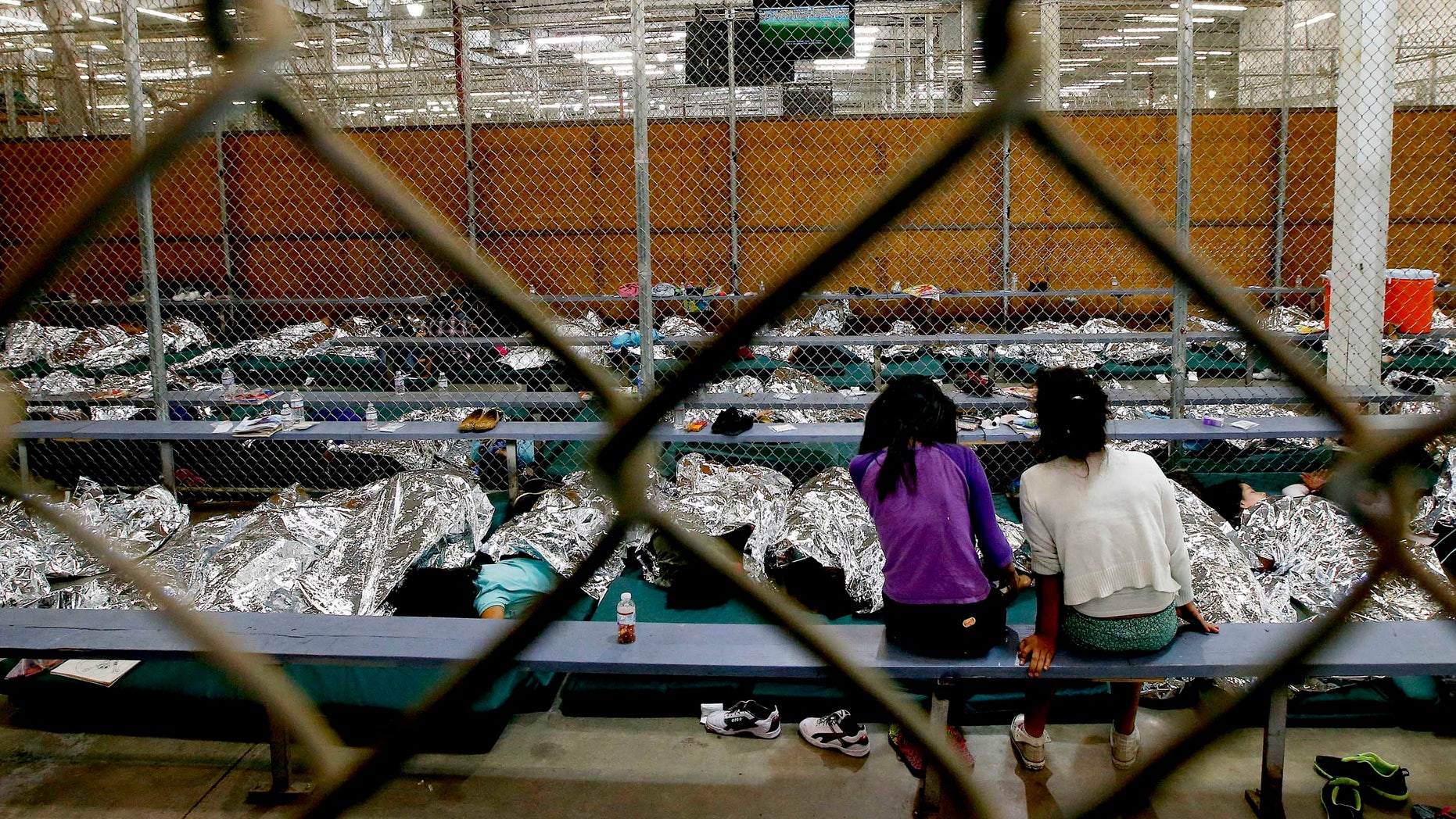 Two young girls watch a World Cup soccer match on a television from their holding area where hundreds of mostly Central American immigrant children are being processed and held at the U.S. Customs and Border Protection Nogales Placement Center on Wednesday, June 18, 2014, in Nogales, Ariz. CPB provided media tours Wednesday of two locations in Brownsville, Texas, and Nogales, that have been central to processing the more than 47,000 unaccompanied children who have entered the country illegally since Oct. 1. (AP Photo/Ross D. Franklin, Pool)