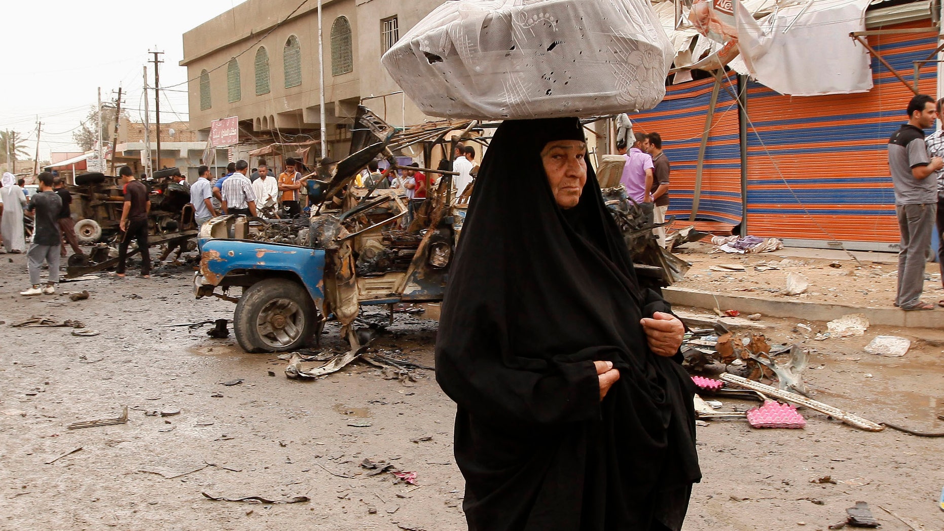 An Iraqi woman, who sells milk, passes by the scene of a car bomb attack in the Kamaliyah neighborhood, a predominantly Shiite area of eastern Baghdad, Iraq, Monday, May 20, 2013. A wave of car bombings across Baghdad's Shiite neighborhoods and in the southern city of Basra killed and wounded scores of people, police said. (AP Photo/ Hadi Mizban)