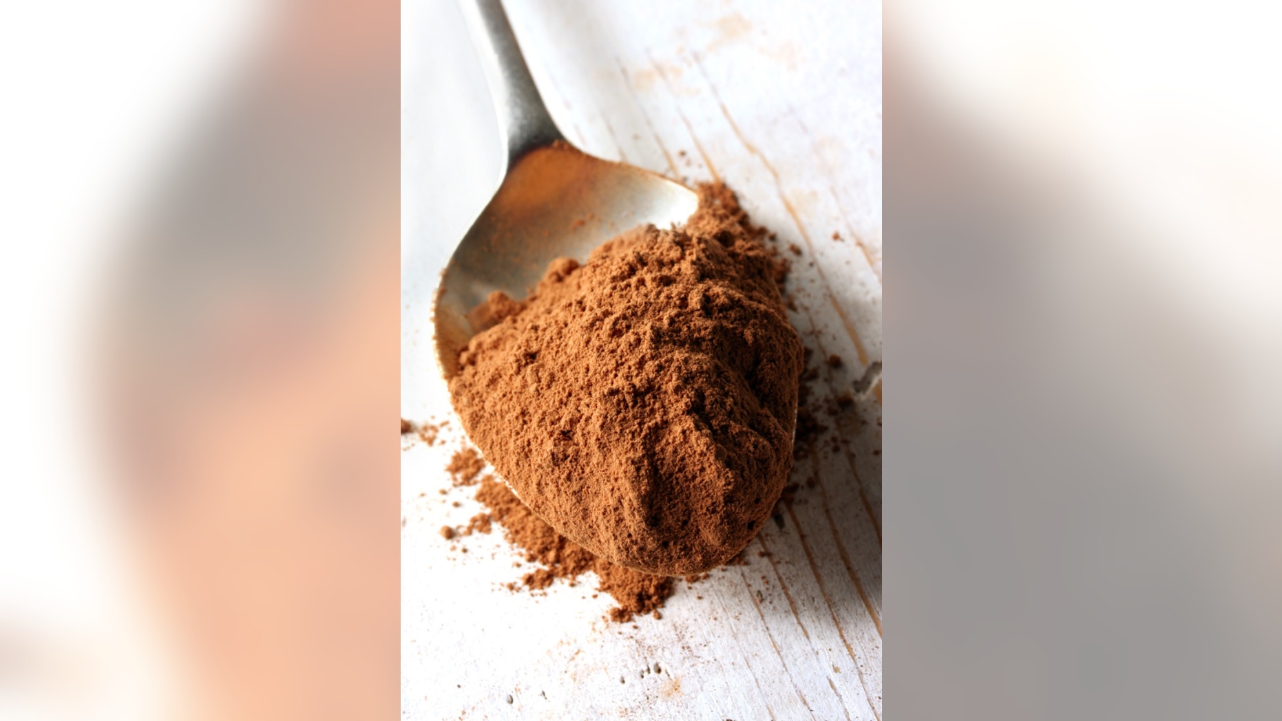 Cocoa powder on an old silver spoon, on rough wooden surface.