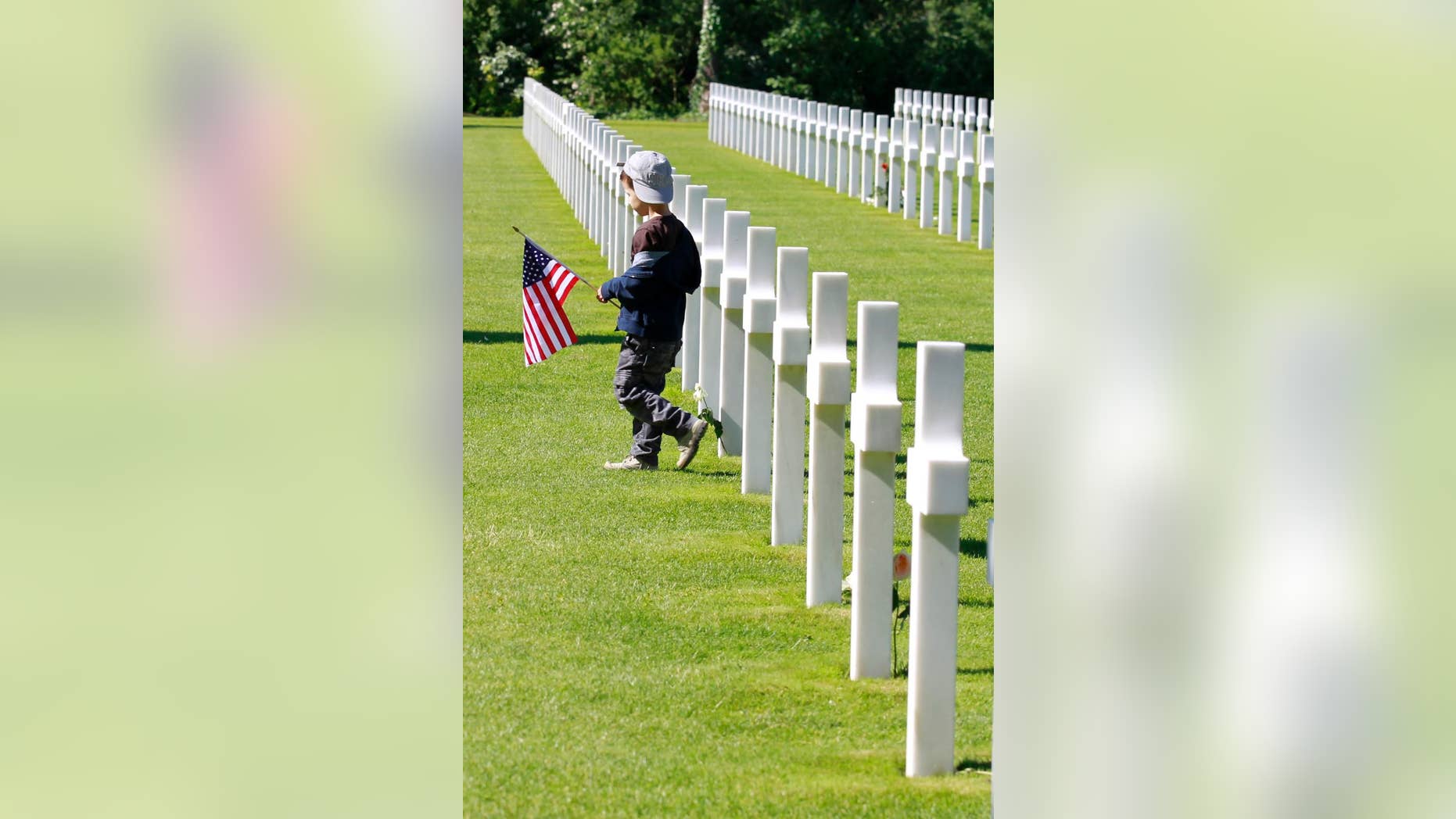 A young visitor carrying the U.S. flag walks among graves at the Colleville American military cemetery, in Colleville sur Mer, western France, Saturday June 6, 2015, on the 71th anniversary of the D-Day landing. D-Day marked the start of a Europe invasion, as many thousands of Allied troops began landing on the beaches of Normandy in northern France in 1944 at the start of a major offensive against the Nazi German forces, an offensive which cost the lives of many thousands. (AP Photo/Remy de la Mauviniere)