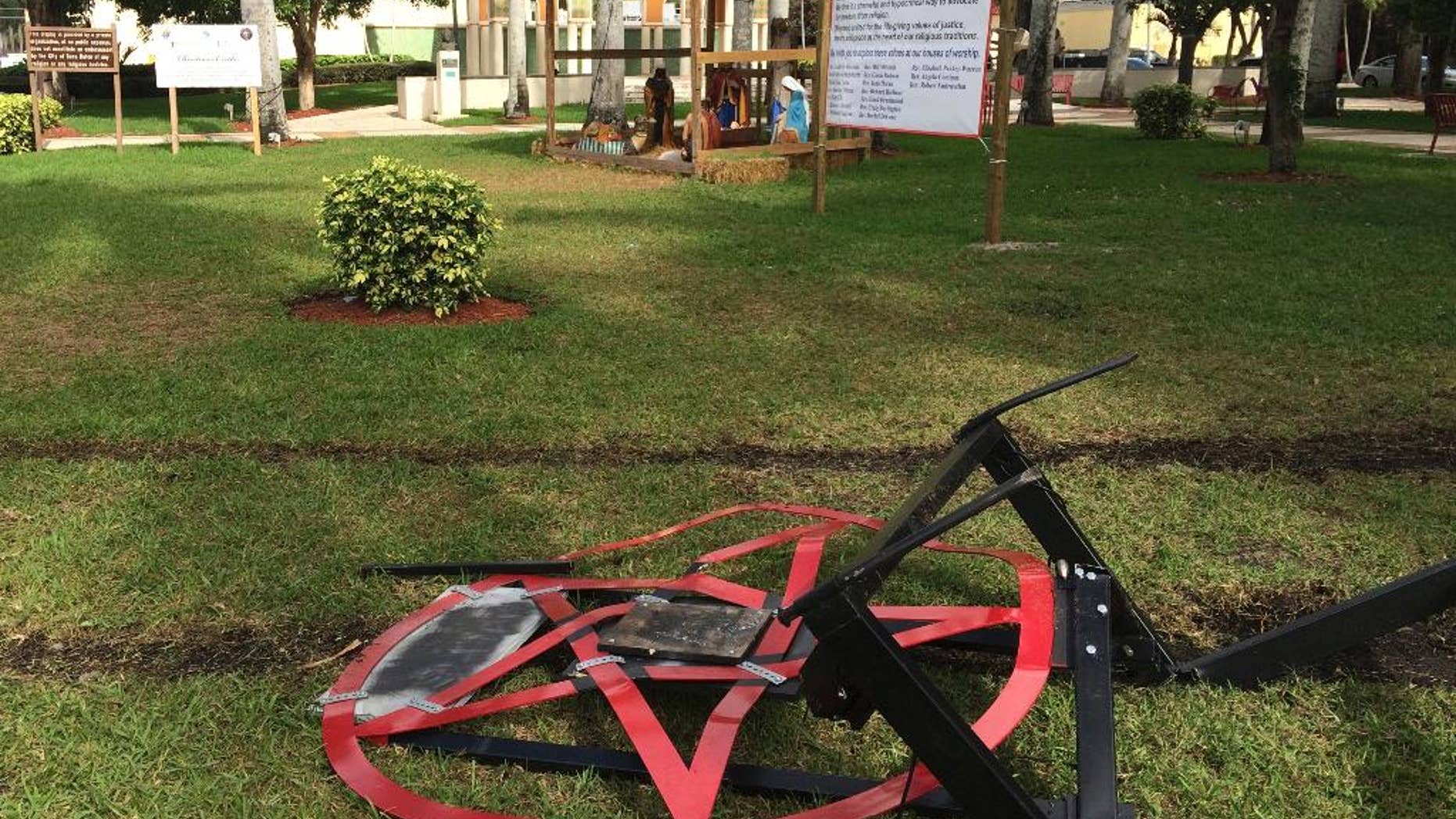 A satanic pentagram erected by atheist Preston Smith lies damaged in Boca Raton's Sanborn Square, Fla. on Tuesday, Dec. 20, 2016. Smith erected the pentagram earlier this month to protest a Nativity scene place in the city-owned square. Vandals apparently dragged down the 300-pound statue using a chain attached to a vehicle. (AP Photo/Terry Spencer)