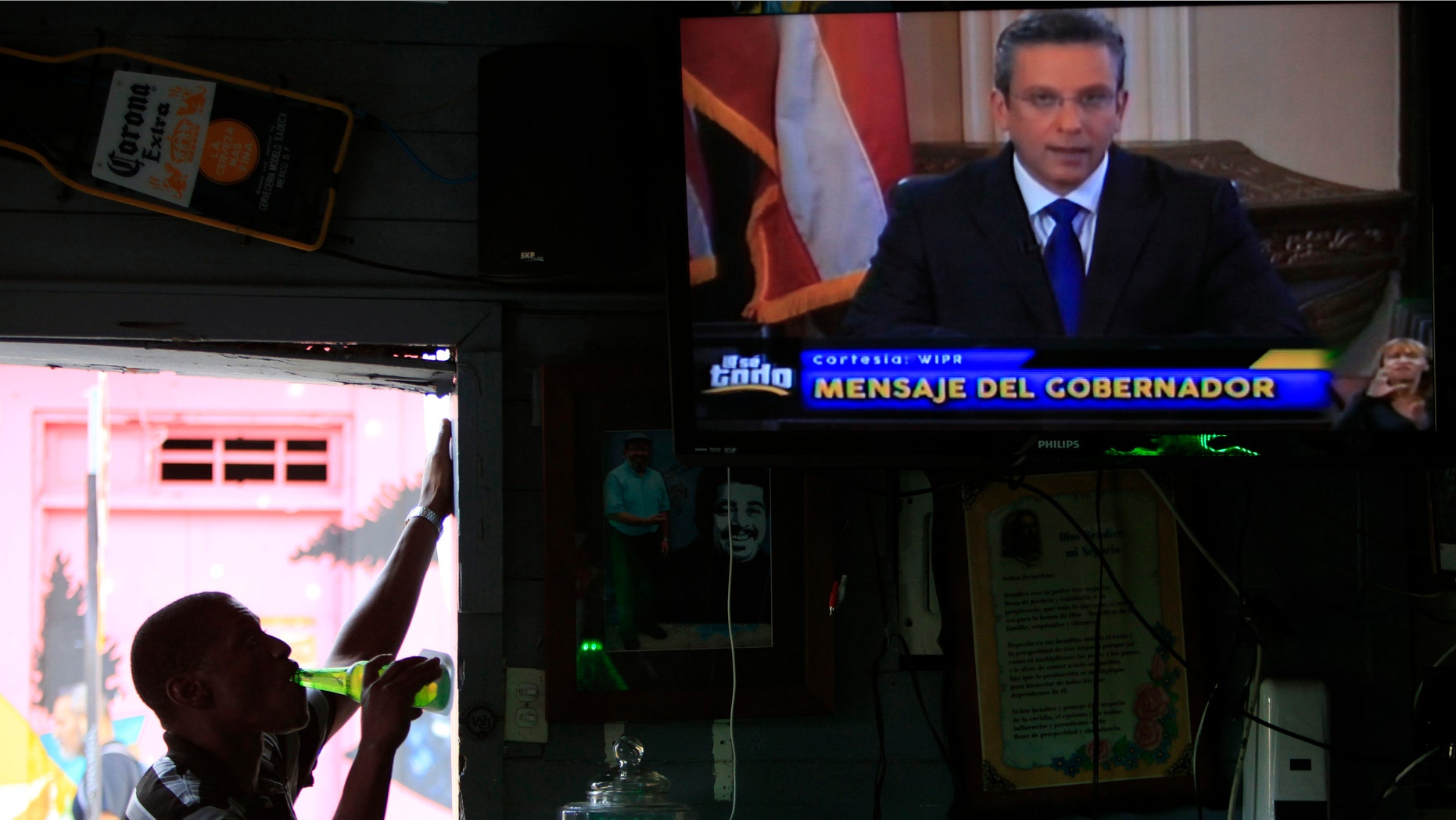 A man drinks a beer in a local bar as he watches Puerto Ricoâs governor Alejandro Garcia Padilla on television delivering an address on the state of the island's finances, in San Juan, Puerto Rico, Monday, June 29, 2015. The governor said that he will form a financial team to negotiate with bondholders on delaying debt payments and then restructuring $72 billion in public debt that he says the island can't repay. (AP Photo/Ricardo Arduengo)