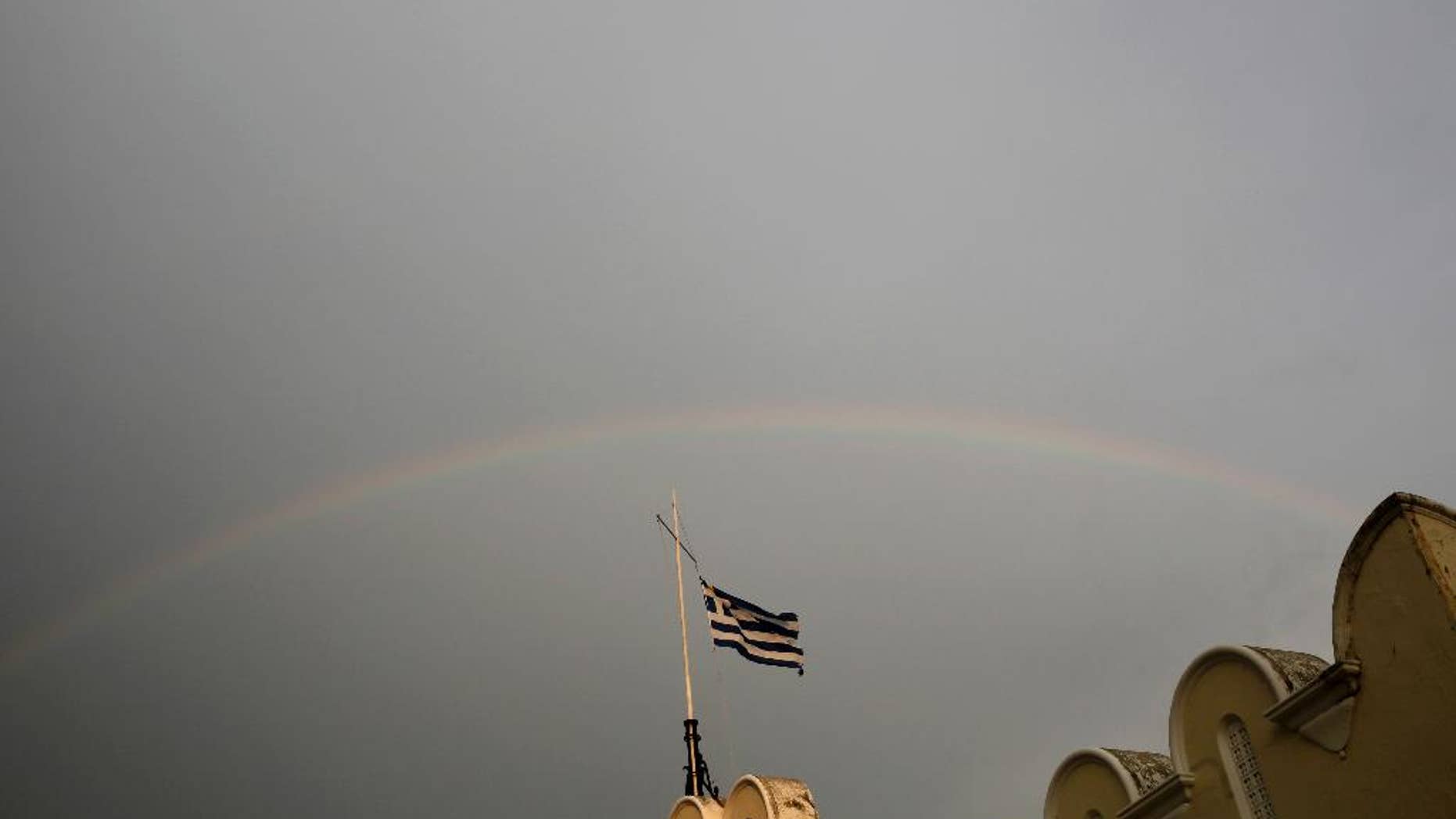 A Greek flag flies on top of the municipality market with rainbow on the background on Kos island, Greece, Friday, May 29, 2015. Bank deposits in Greece have hit their lowest in more than a decade, according to data released Friday, as Greeks concerned about the painfully slow pace of their government's talks with bailout creditors withdrew savings in an orderly but steady flow.(AP Photo/Petros Giannakouris)