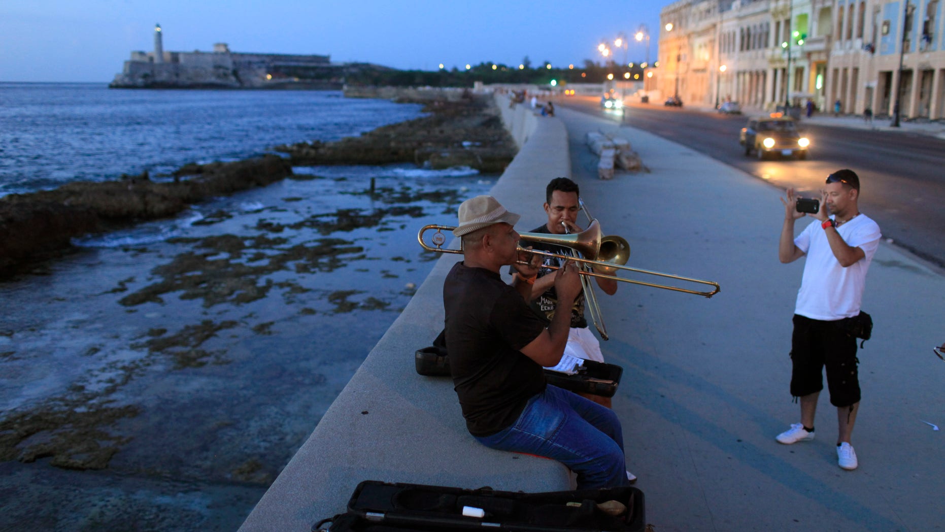 Musicians play trombones as a tourist from Colombia takes their picture along the Malecon in Havana, Cuba.