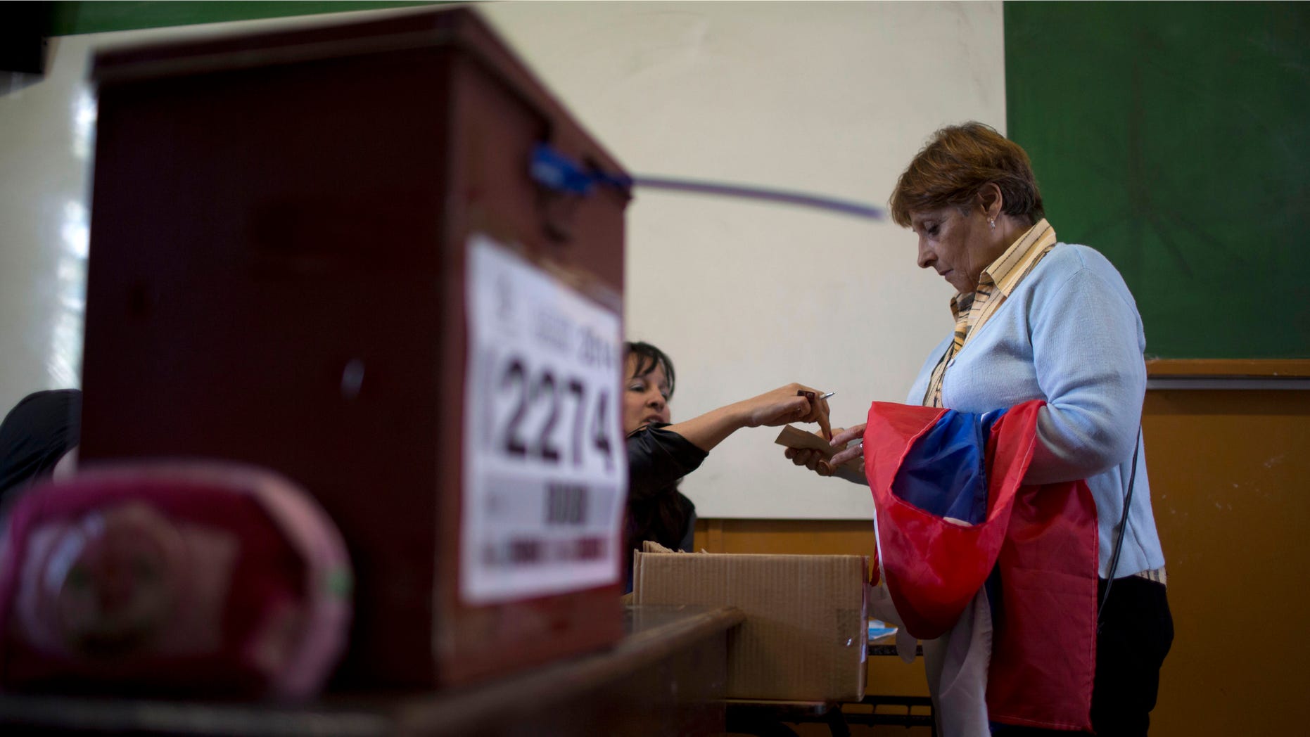 Voter Ana Perez arrives at a polling station with a flag representing the ruling Broad Front party draped over her arm, in Montevideo, Uruguay Sunday, Oct. 26, 2014. Polls suggest that Broad Front candidate Tabare Vazquez, will fall short of the absolute majority, forcing a runoff next month. His main challenger is center-right National Party candidate Luis Alberto Lacalle Pou, the son of a former president. (AP Photo/Natacha Pisarenko)