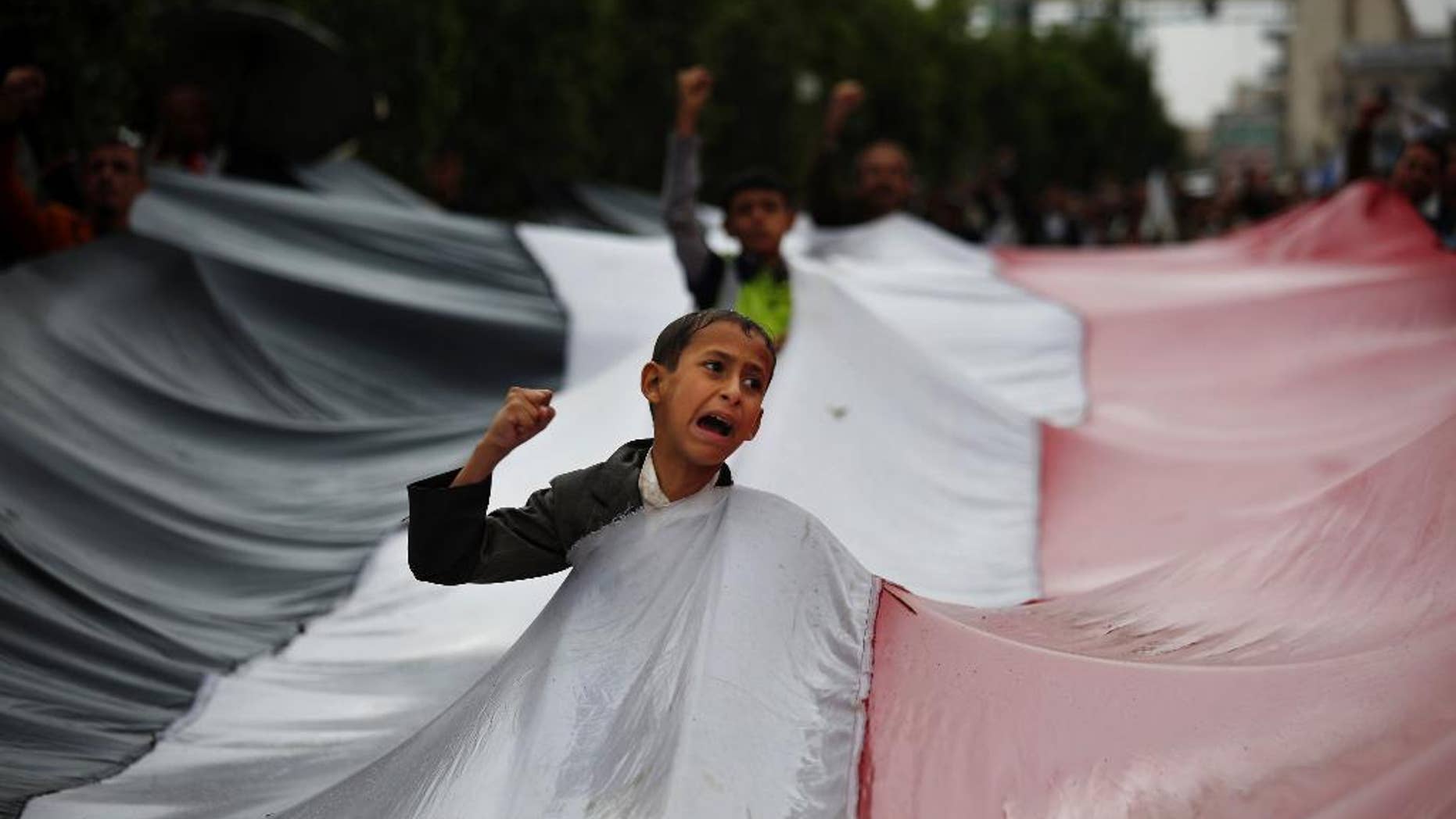 A boy chants slogans through a gap in a national flag raised by Shiite rebels, known as Houthis, during a protest against Saudi-led airstrikes in Sanaa, Yemen, Friday, April 15, 2016. (AP Photo/Hani Mohammed)