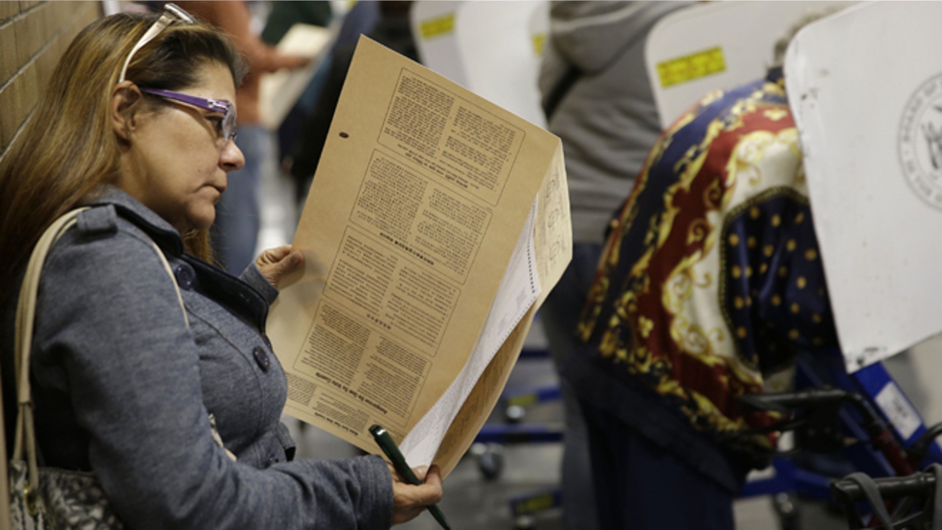 Because all the privacy booths are full, Miriam Rodriguez looks over her ballot while leaning against the wall at a polling site in New York, Tuesday, Nov. 4, 2014. (AP Photo/Seth Wenig)