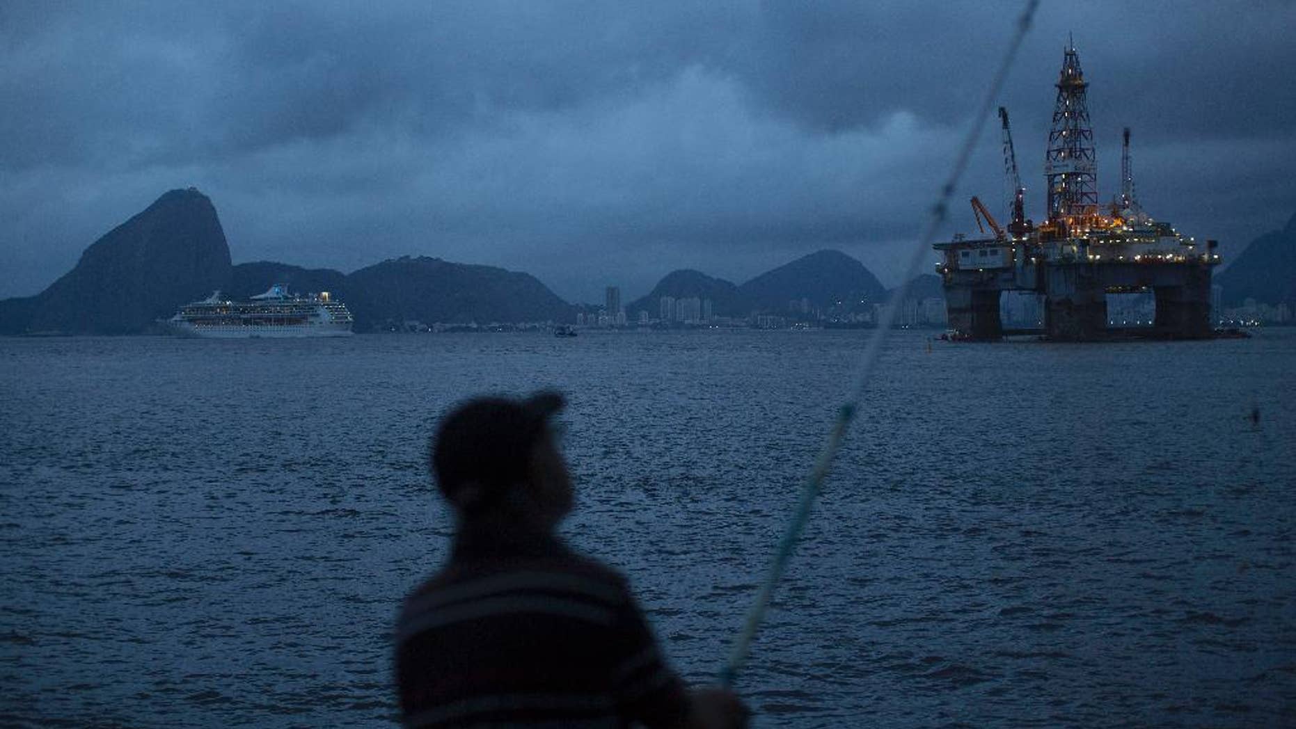 FILE - In this April 21, 2015 file photo, a man fishes in Guanabara Bay where an oil platform floats, backdropped by Sugar Loaf Mountain, left, in Niteroi, Brazil. The Brazilian government on Monday, Sept. 12, 2016 ratified its participation in the Paris Agreement on climate change, a significant step by Latin America’s largest emitter of greenhouse gases that could spur other countries to move forward. (AP Photo/Leo Correa, File)