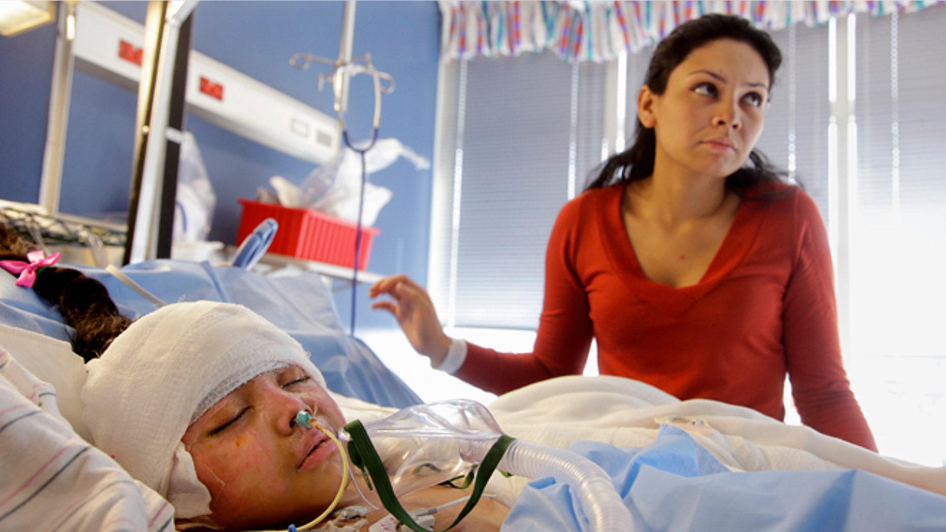 In this Wednesday, March 11, 2015 photo Paola Porter Avila stands over her daughter Paola Matute Porter, 9, in the acute care burn unit of the Shriners Hospitals for Children in Boston. While doctors say Paola Matute's skin grafts are taking well and she is gradually being weaned off pain medication, she will spend a couple more weeks in the hospital before being transferred to a temporary Boston residence to undergo physical therapy. (AP Photo/Stephan Savoia)