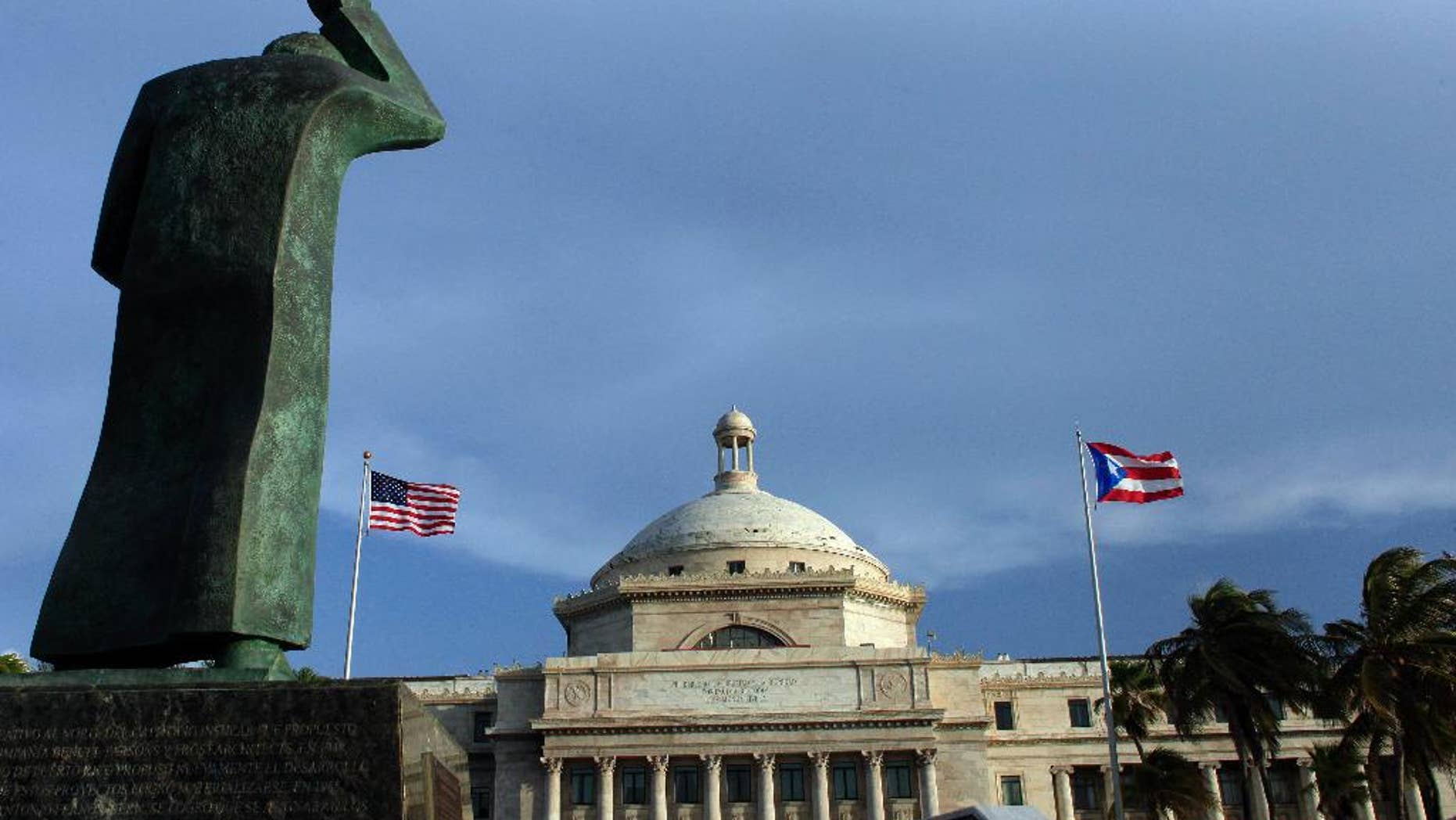 FILE - In this July 29, 2015 file photo, a bronze statue of San Juan Bautista stands in front of Puerto Rico’s capitol flanked by U.S. and Puerto Rican flags, in San Juan. A federal control board on Friday, Sept. 30, 2016, took over Puerto Rico's finances and several government agencies for the first time in the U.S. territory's history in a bid to haul the island out of an acute economic crisis. (AP Photo/Ricardo Arduengo, File)
