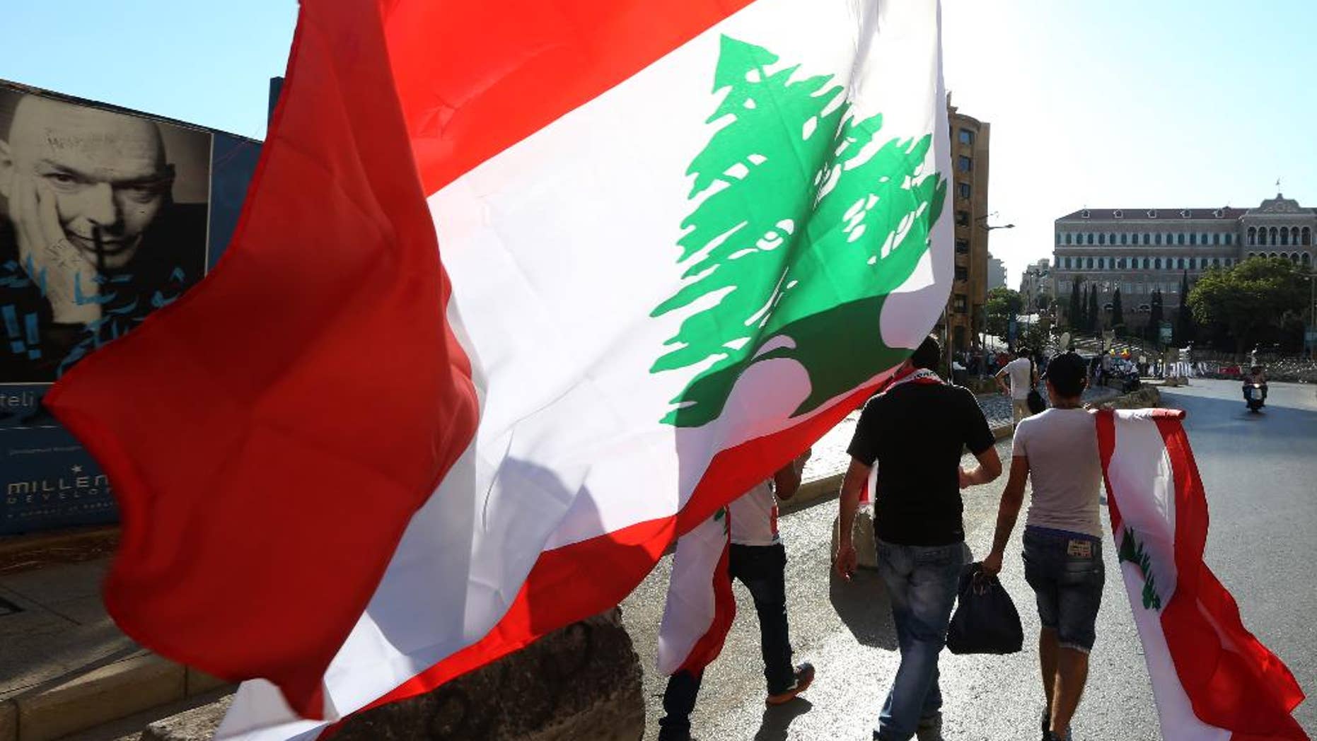 Lebanese anti-government protesters carry Lebanese flags as they walk towards the government building, background, during a demonstration against the trash crisis and government corruption, in downtown Beirut, Lebanon, Saturday, Aug. 29, 2015. Hundreds of people began gathering Saturday amid tight security in downtown Beirut, ahead of a major rally that is expected to be the largest of protests that began last week. The government's failure to resolve the crisis has evolved into wider protests against a political class that has dominated Lebanon since the end of the country's civil war in 1990. (AP Photo/Bilal Hussein)