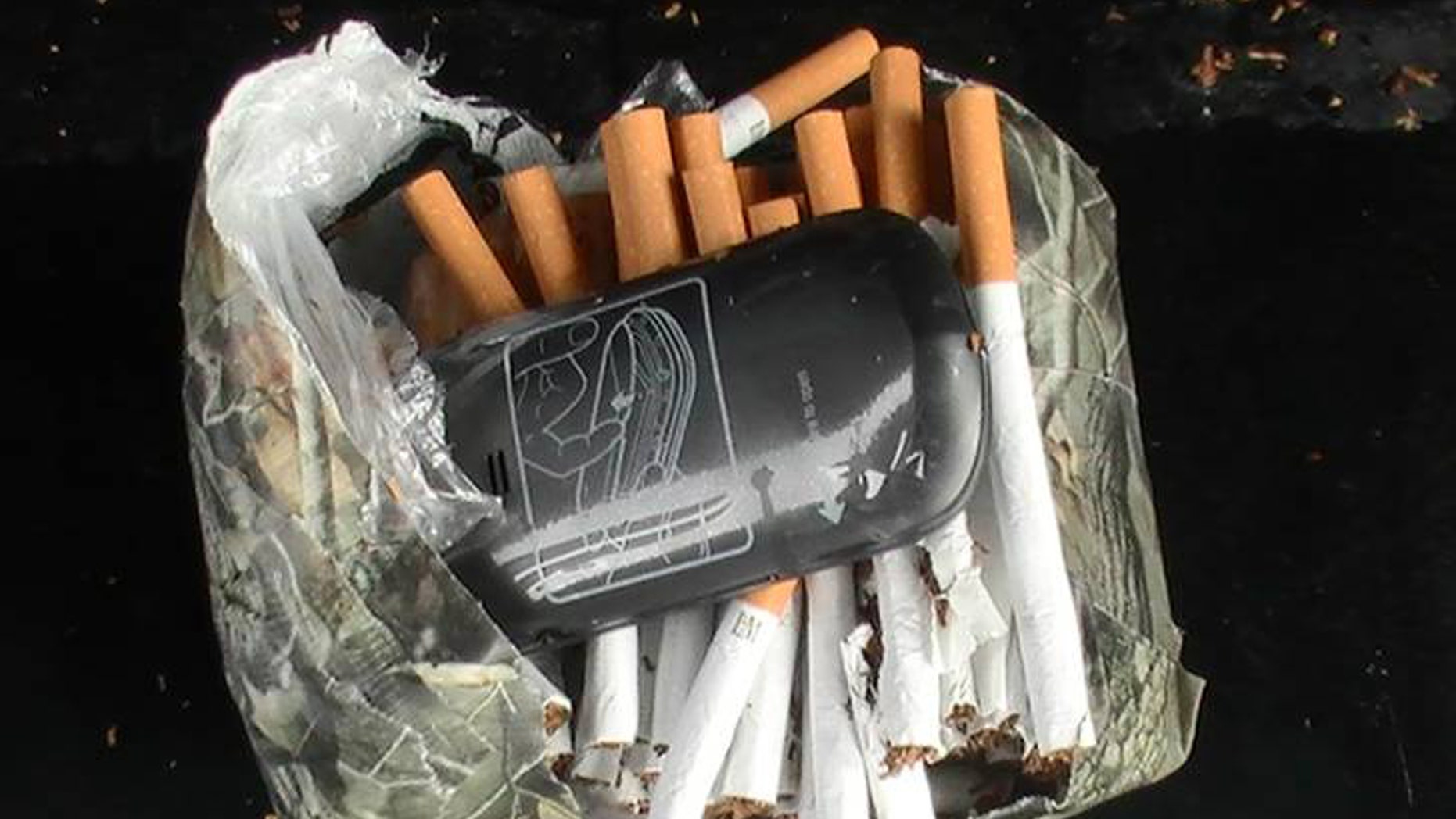 This undated photo mprovided by the Florida Department of Corrections shows a cellphone and cigarettes that were found inside a camouflage package, January 25, 2014, near an undisclosed Florida state prison. Prison officials in Florida and nationwide are fighting a different type of contraband being smuggled to inmates: cellphones. They're being hidden in babies' diapers, Ramen Noodle Soup packages, footballs, soda cans and body cavities.Two murderers used cellphones to plan their escape from a Florida prison last year where the state confiscated 11 cellphones per day in its prisons. (AP Photo/Florida Department of Corrections)