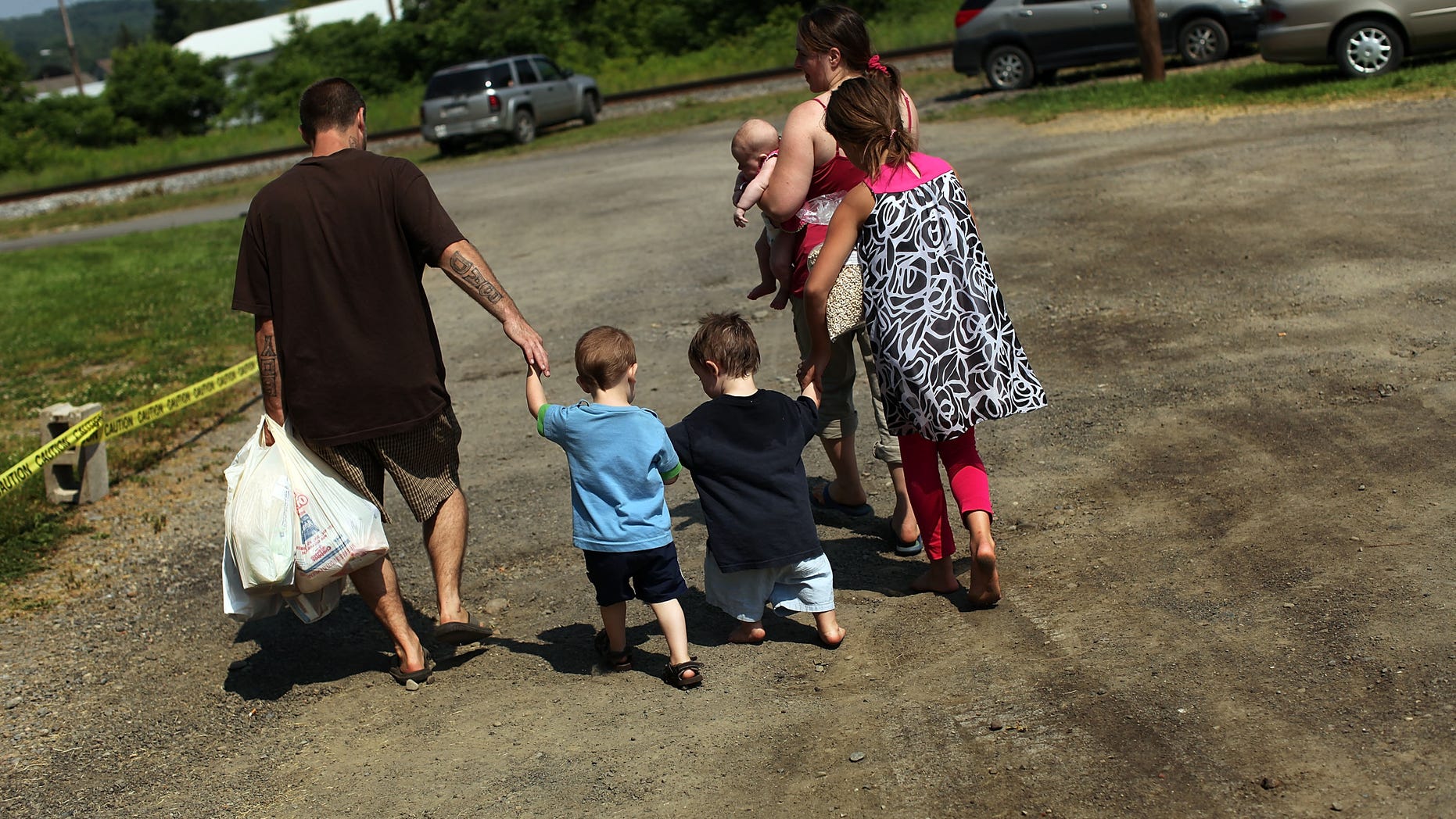 OSWEGO, NY - JUNE 20: Members of the Dolan family walk home with bags of food after a food distribution by the Food Bank of the Southern Tier Mobile Food Pantry on June 20, 2012 in Oswego, New York. The mobile food pantry program was introduced in 2007 in the Southern Tier of New York and covers nearly 4,000 predominately rural miles. The converted beverage truck delivers fresh produce, dairy products and other grocery items to individuals and families in need. The pantry typically distributes for a period of two hours and provides 100 to 160 families with food. According to the 2010 Census, 15.72% the population serviced by the mobile pantry live at or below the federal poverty level. According to statistics presented at a recent U.S. Senate committee hearing, almost one in seven Americans are living below the poverty line with a significant number of them being children. (Photo by Spencer Platt/Getty Images)