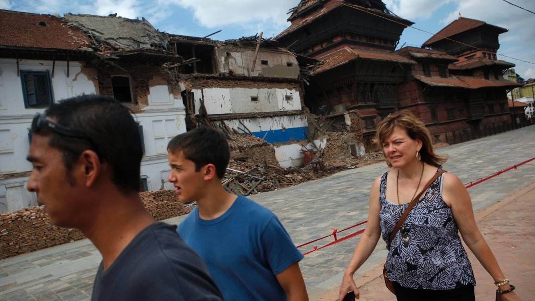 FILE- In this June 15, 2015 file photo, tourists walk near damaged buildings at Basantapur Durbar Square in Kathmandu, Nepal. Nepal's government is urging other countries to lift travel advisories that discourage their citizens from visiting the Himalayan nation following a devastating earthquake in April that killed thousands of people, a government minister said Wednesday, July 15, 2015. (AP Photo/Niranjan Shrestha, file)