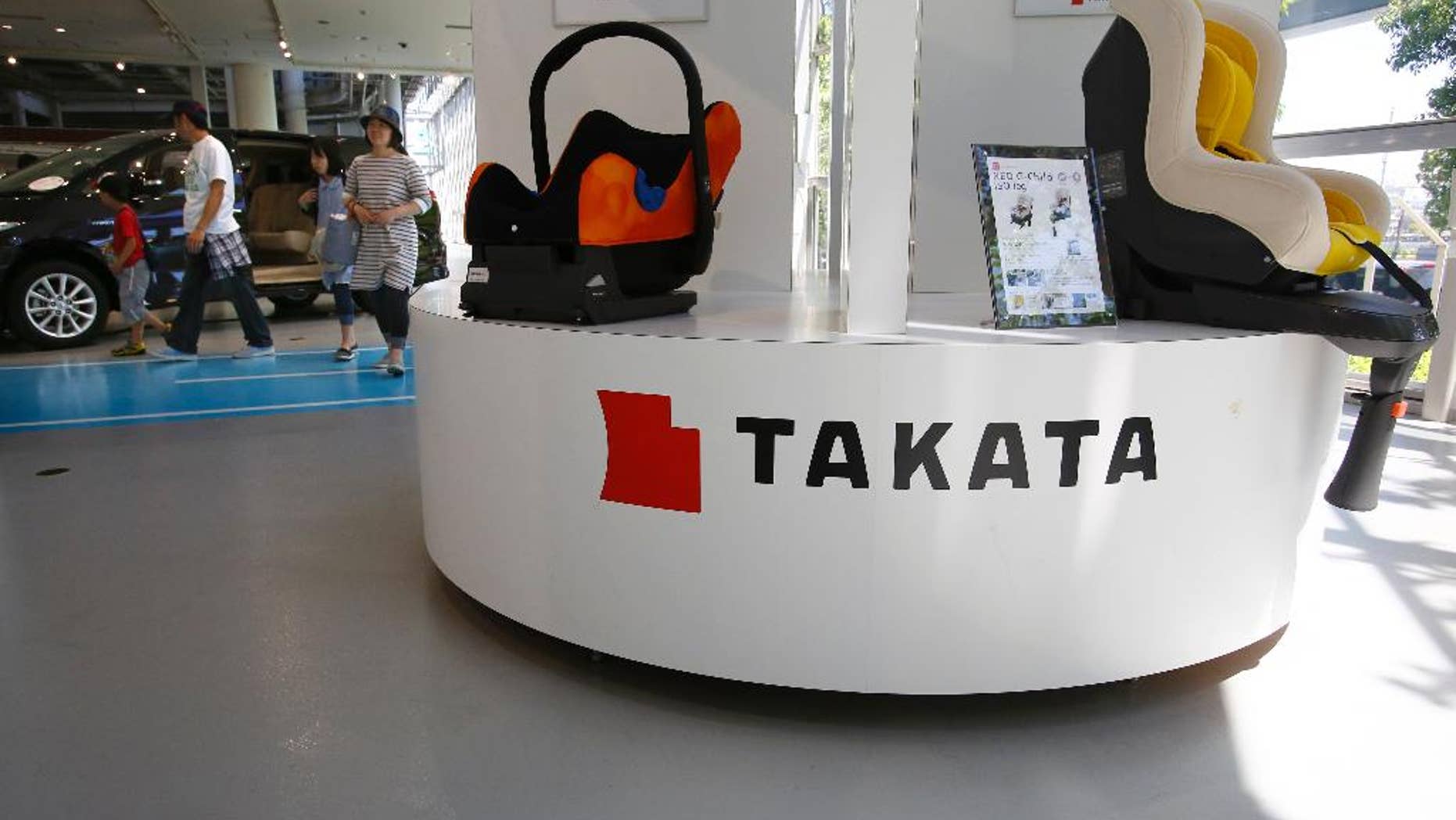 In this Wednesday, May 4, 2016 photo, a family walk by child seats manufactured by Japanese auto parts maker Takata Corp. at an automaker's showroom in Tokyo. Takata, which also makes seat belts, is expecting a loss instead of a profit for the fiscal year that ended in March because of ballooning costs from a massive global air-bag recall. Tokyo-based Takata, which is set to give its earnings report Wednesday, May 11, said Monday, May 9, it is projecting an annual net loss of 13 billion yen ($120 million). (AP Photo/Shizuo Kambayashi)