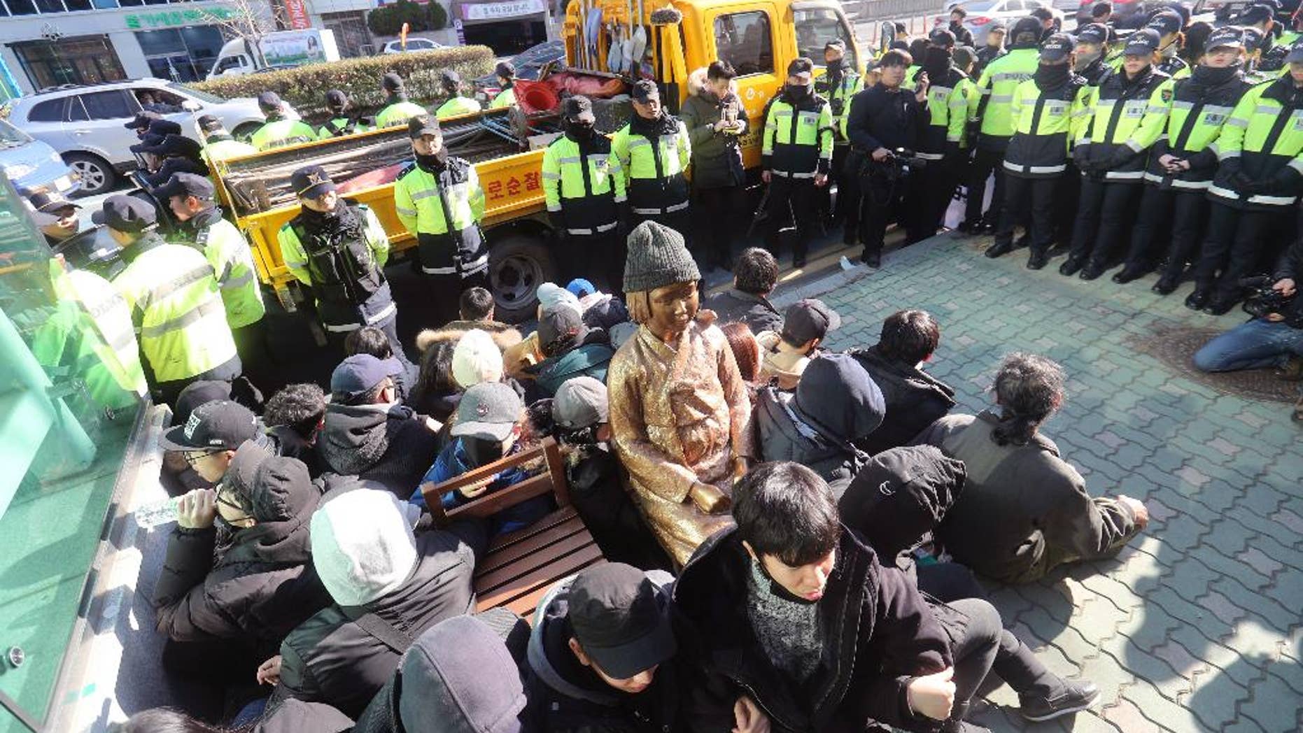 In this Dec. 28, 2016, photo, members of civic groups sit around a comfort-woman statue after they set up in front of the Japanese consulate as police officers surround them in Busan, South Korea. Japan is recalling its ambassador to South Korea Friday, Jan. 6, 2017 in response to the placing of the statue. Many Koreans and other women in Asia were forced to work in brothels for the Japanese military during World War II in what was called the "comfort-woman" system. (Kim Sun-ho/Yonhap via AP)