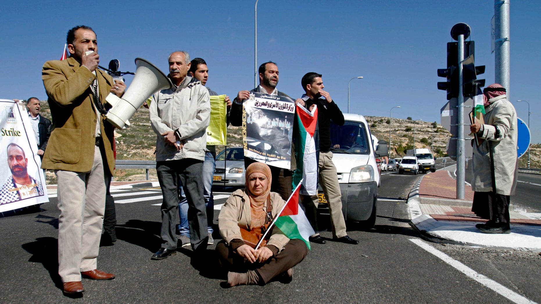 Palestinians briefly block a main West Bank road during a demonstration calling for the release of prisoners jailed in Israel near Bethlehem, Monday, Feb. 18, 2013. Israel is holding some 4,500 Palestinians for charges ranging from throwing stones to undertaking deadly militant attacks. Their incarceration is a sensitive issue for Palestinians, who see them as heroes of the Palestinian liberation struggle. Posters show the face one detainee and slogans calling for the release of prisoners. (AP Photo/Nasser Shiyoukhi)