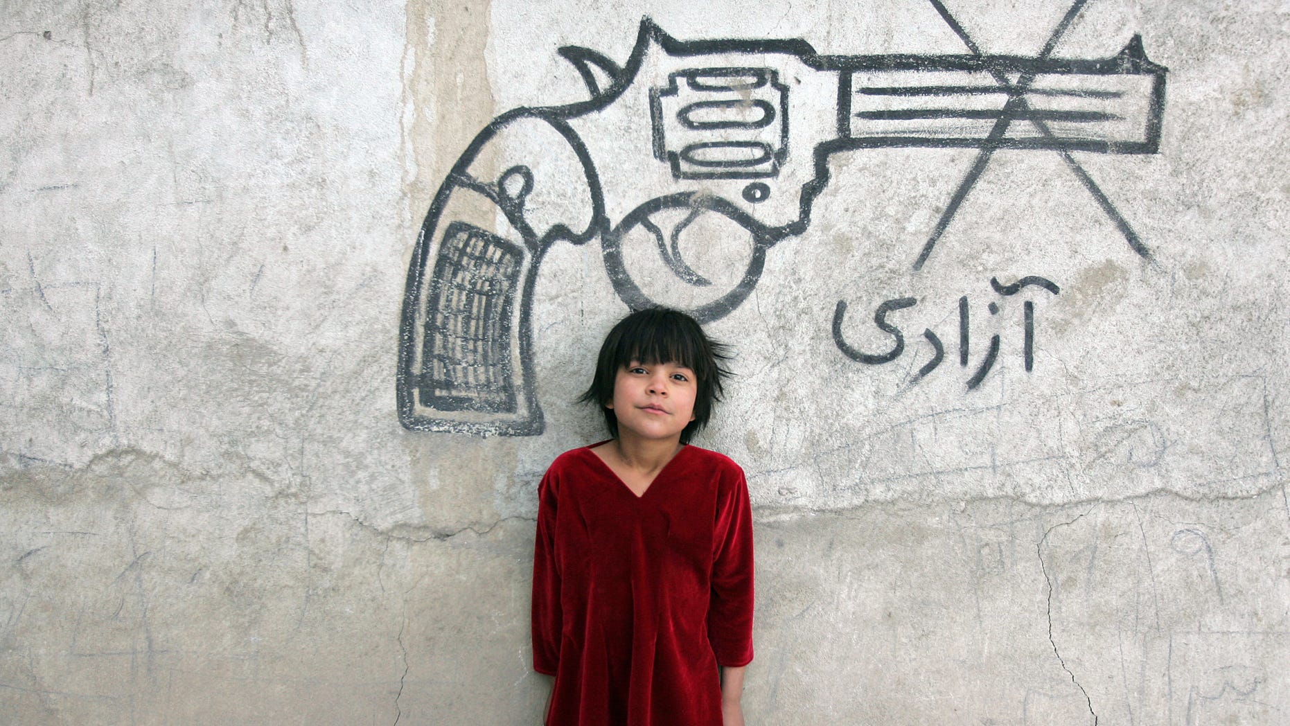 An Afghan child poses for a photograph beneath graffiti of a pistol, with writing that reads, "freedom," in Kabul, Afghanistan, Sunday, Feb. 10, 2013. (AP Photo/Ahmad Nazar)
