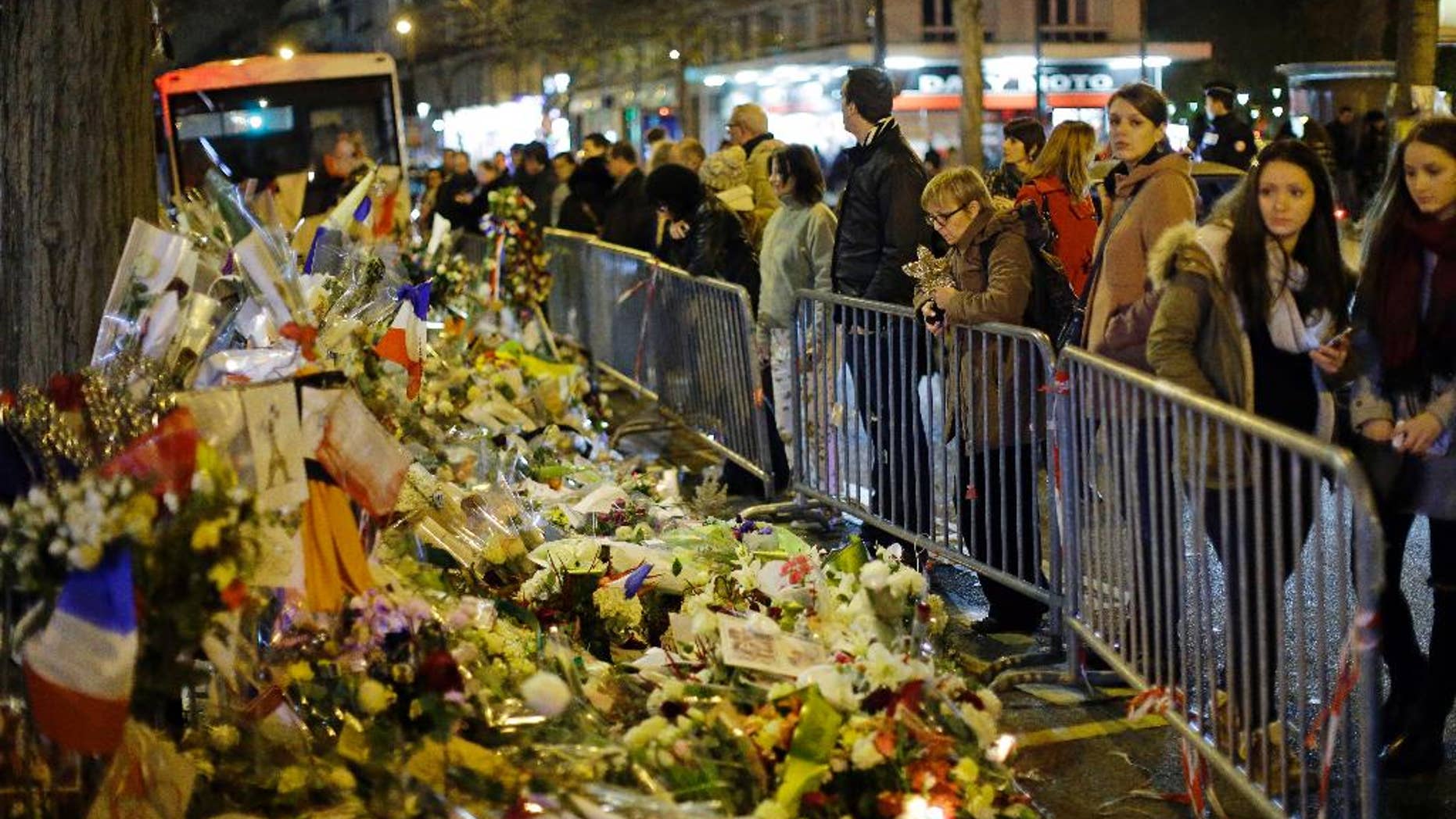 People look at the floral tributes placed to honour the victims of the Paris attacks across from the Bataclan concert hall in Paris Saturday, Dec. 12, 2015. (AP Photo/Matt Dunham)