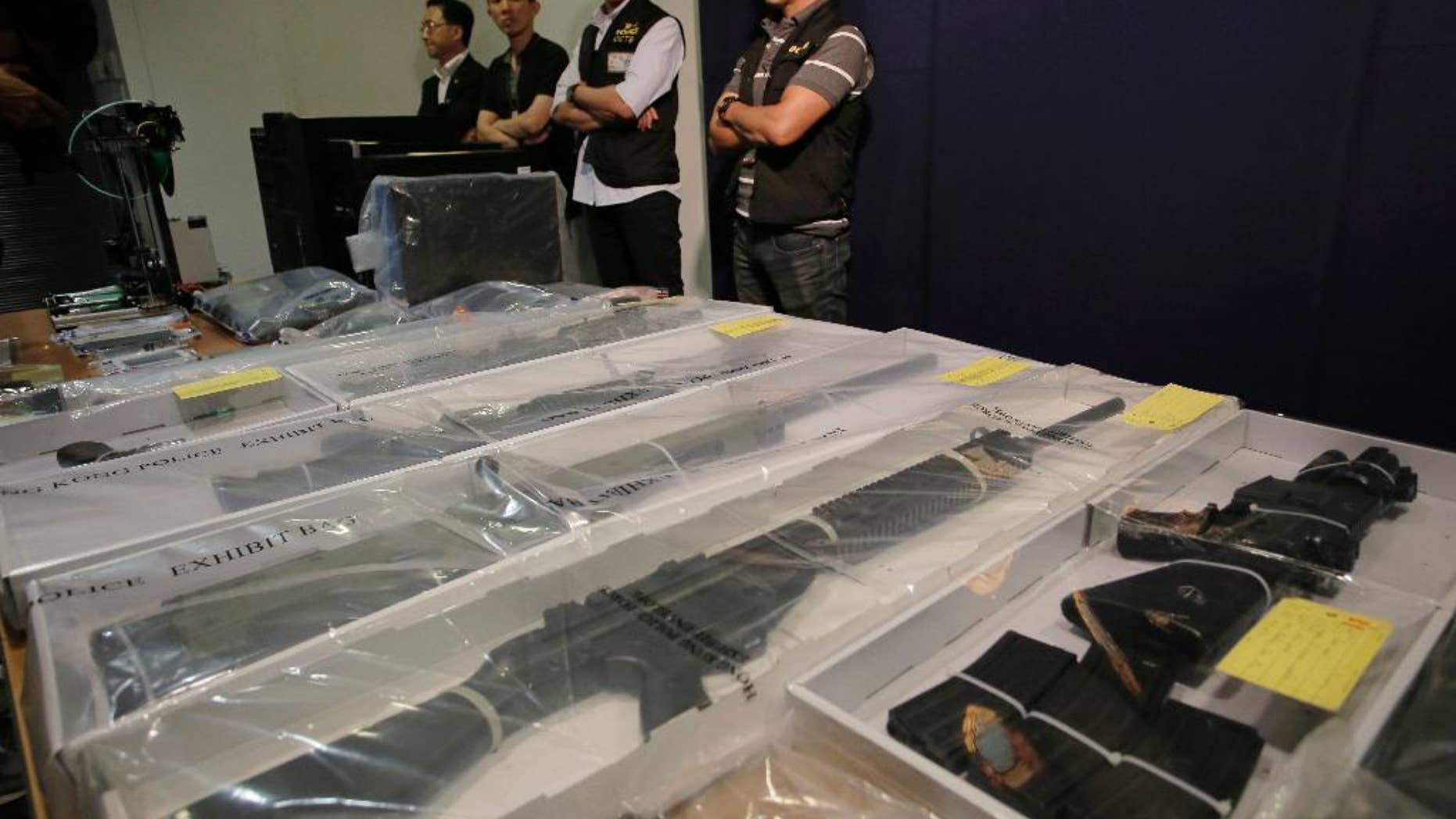 Plain clothed policemen stand guard in front of some air rifles and other evidences during a press conference in Hong Kong, Monday, June 15, 2015. Hong Kong police say they have arrested nine people, members of a local radical group and seized materials for making explosives. (AP Photo/Vincent Yu)
