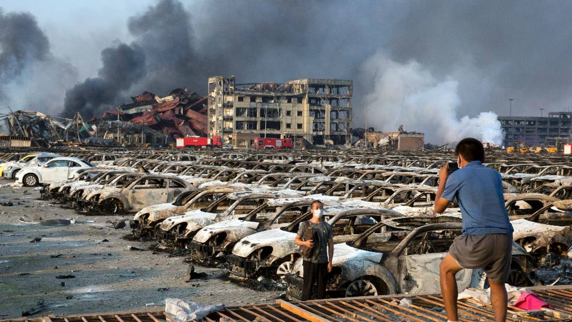 In this photo taken Thursday, Aug. 13, 2015, a man takes photo for another near charred remains of new cars at a parking lot near the site of a warehouse explosion in northeastern China's Tianjin municipality. People recently punished in China's campaign against online rumors include those who circulated an inflated death toll in the Tianjin blasts and who alleged a man committed suicide because of the country's stock market woes, state media reported Monday, Aug. 31, 2015.(AP Photo/Ng Han Guan)