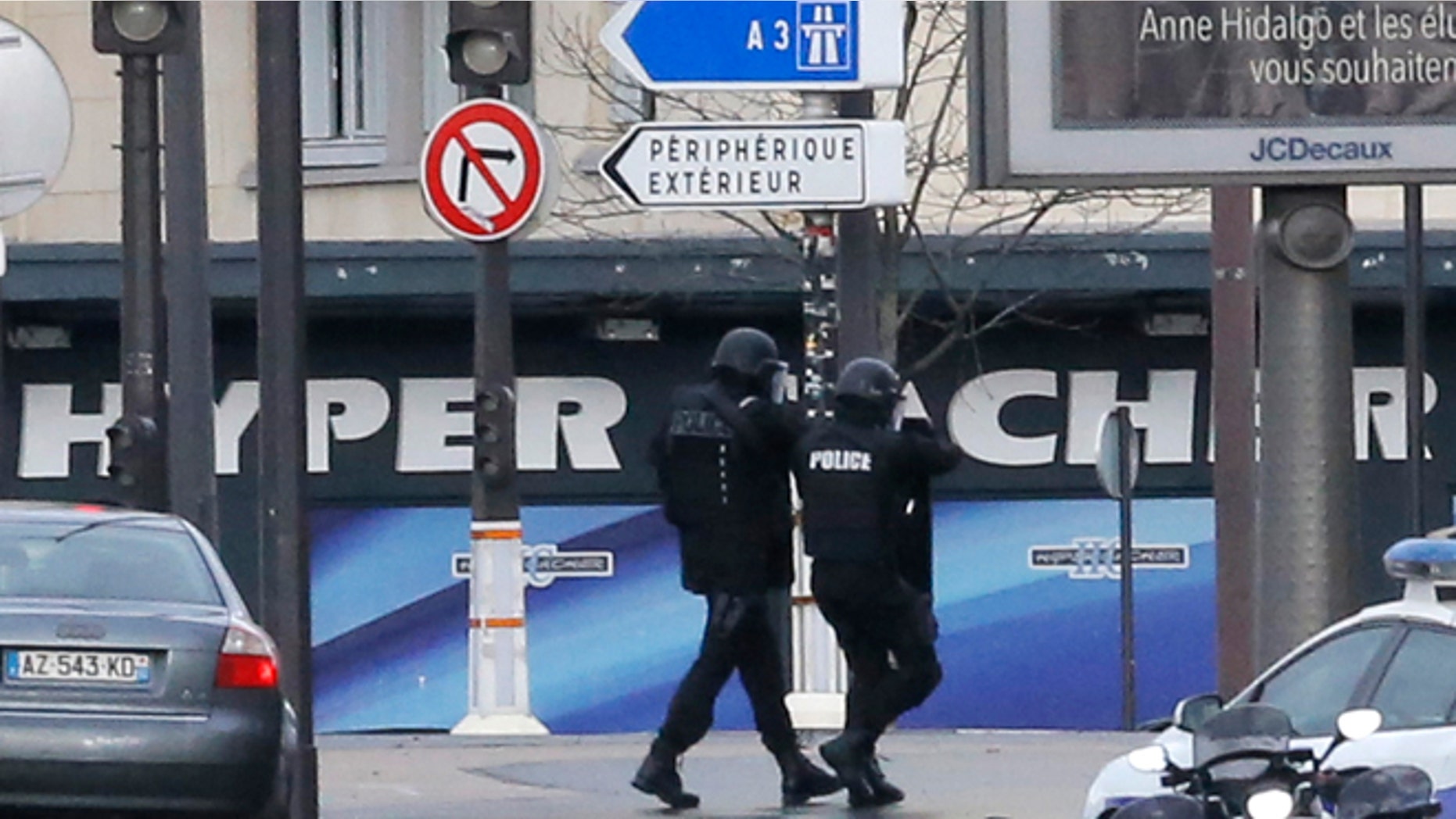 Jan.9, 2015: Police officers walk in front of a hostage-taking situation at a kosher market, seen in blue in background, in Paris, Friday . A police official says the man who has taken at least five people hostage in a kosher market in Paris appears linked to the newsroom massacre earlier this week that left 12 people dead.