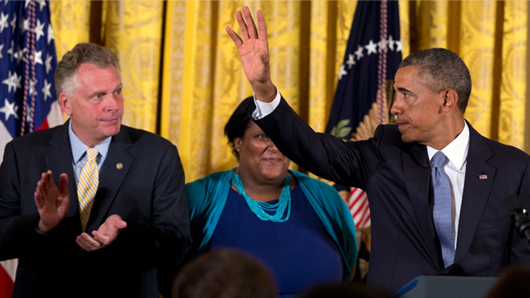 July 21, 2014: Virginia Governor Terry McAuliffe, left, applauds as President Obama waves after signing an executive order to protect LGBT employees from federal workplace discrimination in the East Room of the White House in Washington. Obama's executive order prohibits discrimination against gay and transgender workers in the federal government and its contracting agencies, without a new exemption that was requested by some religious organizations.