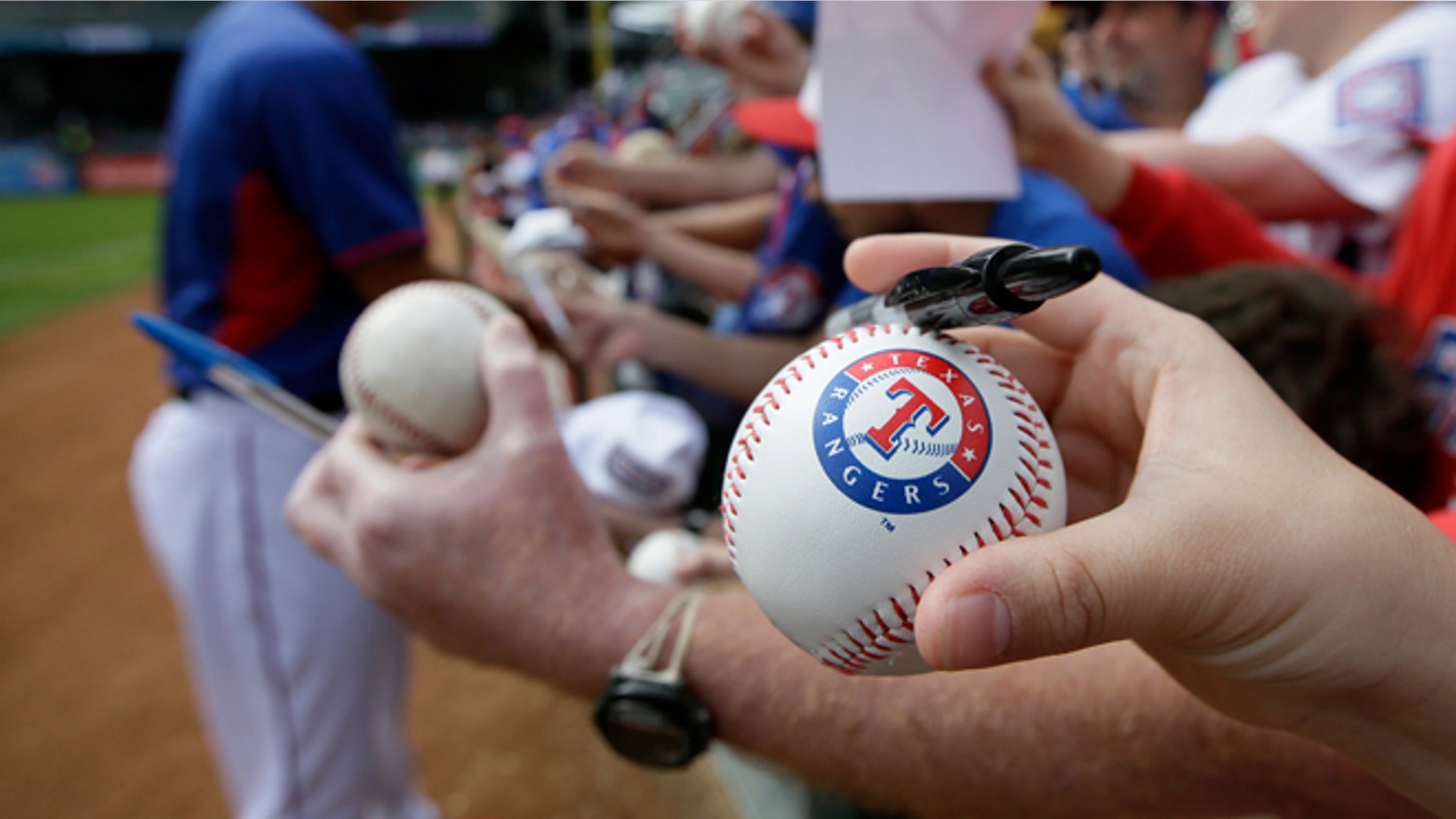 FILE -- March 31, 2014: A fan holds a Texas Rangers stamped baseball waiting for a autograph from Yu Darvish of Japan before a baseball game against the Philadelphia Phillies in Arlington, Texas.