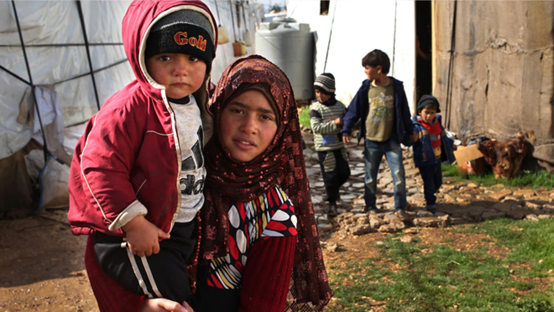FILE -- March 12, 2014: A Syrian girl, foreground, carries her brother and walks between tents with other children, background, on their way to a makeshift school at their refugee encampment in the Lebanese-Syrian border town of Majdal Anjar, eastern Bekaa valley, Lebanon. More than 2 million of those who should be in school remain in Syria, where classrooms have been bombed, used as shelters or turned into military barracks. Another 300,000 Syrian children don’t attend school in Lebanon, along with some 93,000 in Jordan, 78,000 in Turkey, 26,000 in Iraq and 4,000 in Egypt, UNICEF officials in Geneva said. Those numbers likely are higher, as UNICEF can’t count the children whose parents didn’t register with the United Nations refugee agency.