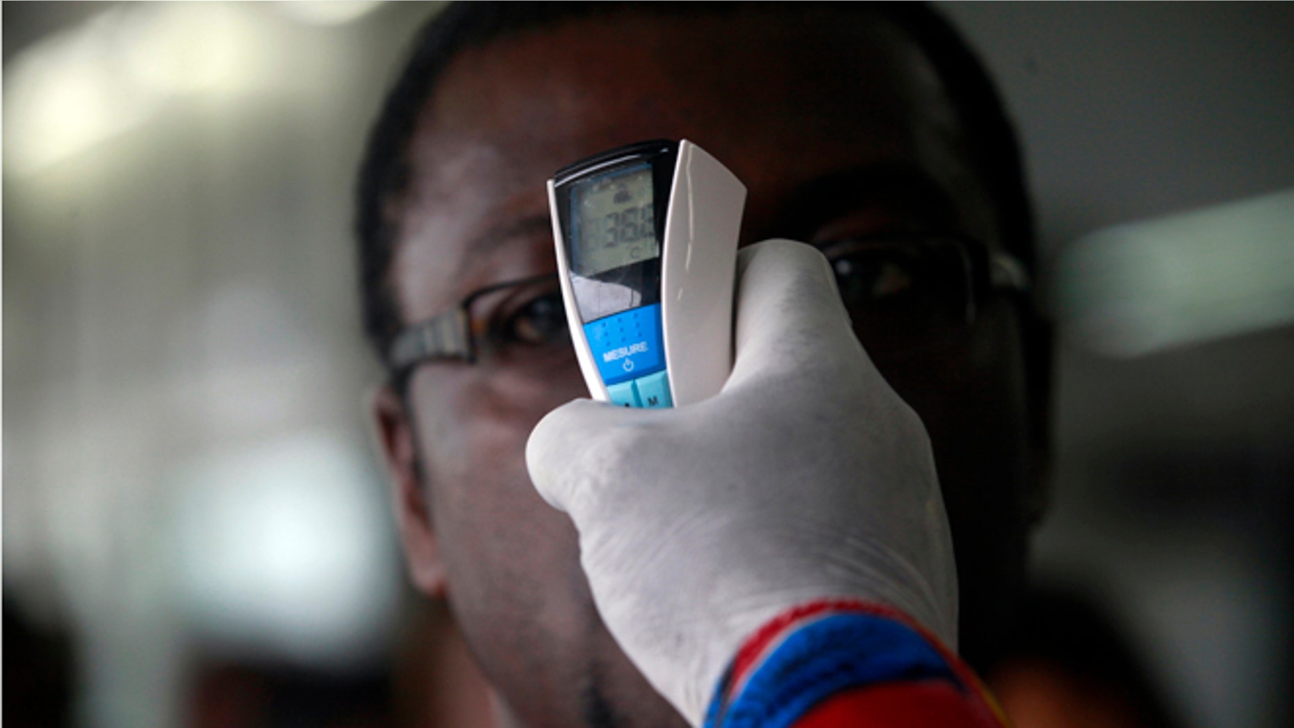 A health worker takes a passenger's temperature with an infrared digital laser thermometer at the Felix Houphouet Boigny international airport in Abidjan August 13, 2014. Ivory Coast on Monday banned air travellers from Guinea, Liberia and Sierra Leone, the three countries worst-hit by the Ebola outbreak, and ordered its flagship carrier Air Cote d'Ivoire to cease flights to and from them. Ivory Coast has not registered any cases but is seen as vulnerable given its shared borders with Guinea and Liberia. REUTERS/Luc Gnago