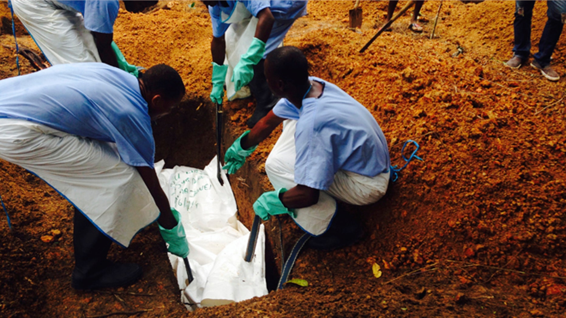 Volunteers lower a corpse, which is prepared with safe burial practices to ensure it does not pose a health risk to others and stop the chain of person-to-person transmission of Ebola, into a grave in Kailahun July 18, 2014. REUTERS/WHO/Tarik Jasarevic/Handout via Reuters