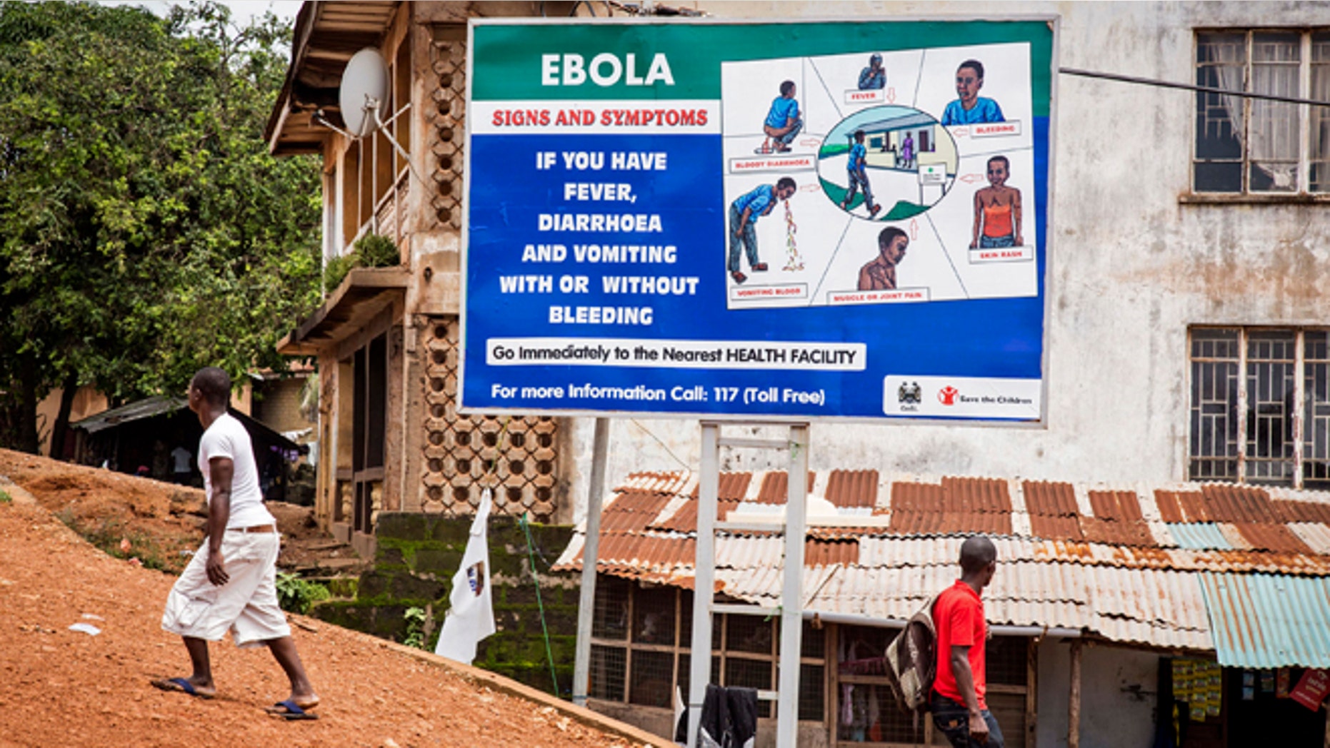People walk past a billboard encouraging people suffering from symptoms linked to Ebola to present themselves at a health facility for treatment in Freetown, Sierra Leone, Thursday, Aug. 7, 2014. (AP Photo/ Michael Duff)