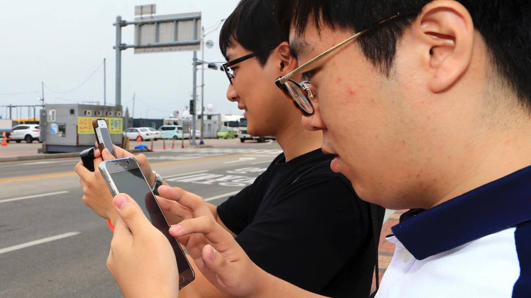 In this July 13, 2016 photo, two South Koreans play the Pokemon Go game with their mobile phones in Sokcho, South Korea. The seaside South Korean city of Sokcho is enjoying a surge of visitors who are wandering the streets at all hours as they look at their smartphones. It appears to be the only place in the country where Pokemon Go players can chase the mobile game's virtual monsters. (Lee Jong-hun/Yonhap via AP)