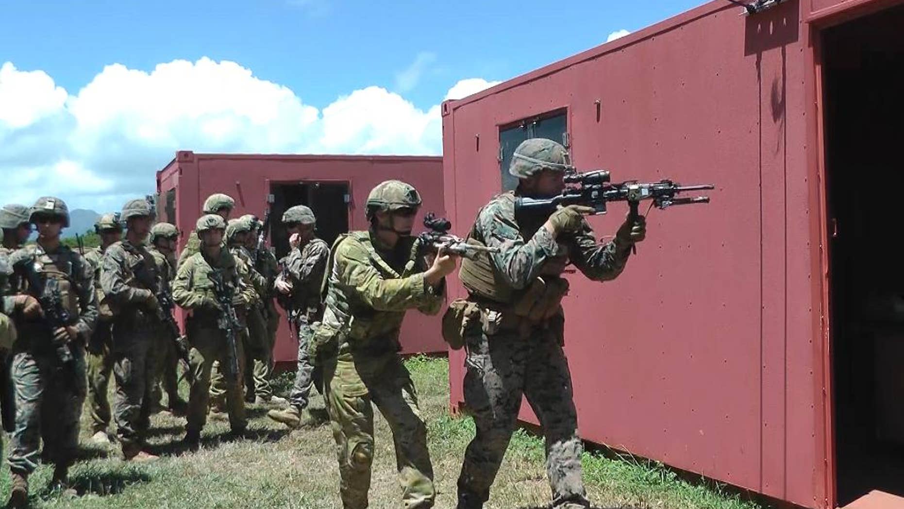 In this Thursday, July 7, 2016 photo, an Australian soldier, center left, and a U.S. Marine, right, get ready to raid a building at a mock urban combat training center in Kaneohe Bay, Hawaii. Australian soldiers are expected to lead a battalion of troops in the storming of a Hawaii beach during the world's largest maritime exercises this month, displaying the amphibious military skills they've been building up in recent years. (AP Photo/Audrey McAvoy)