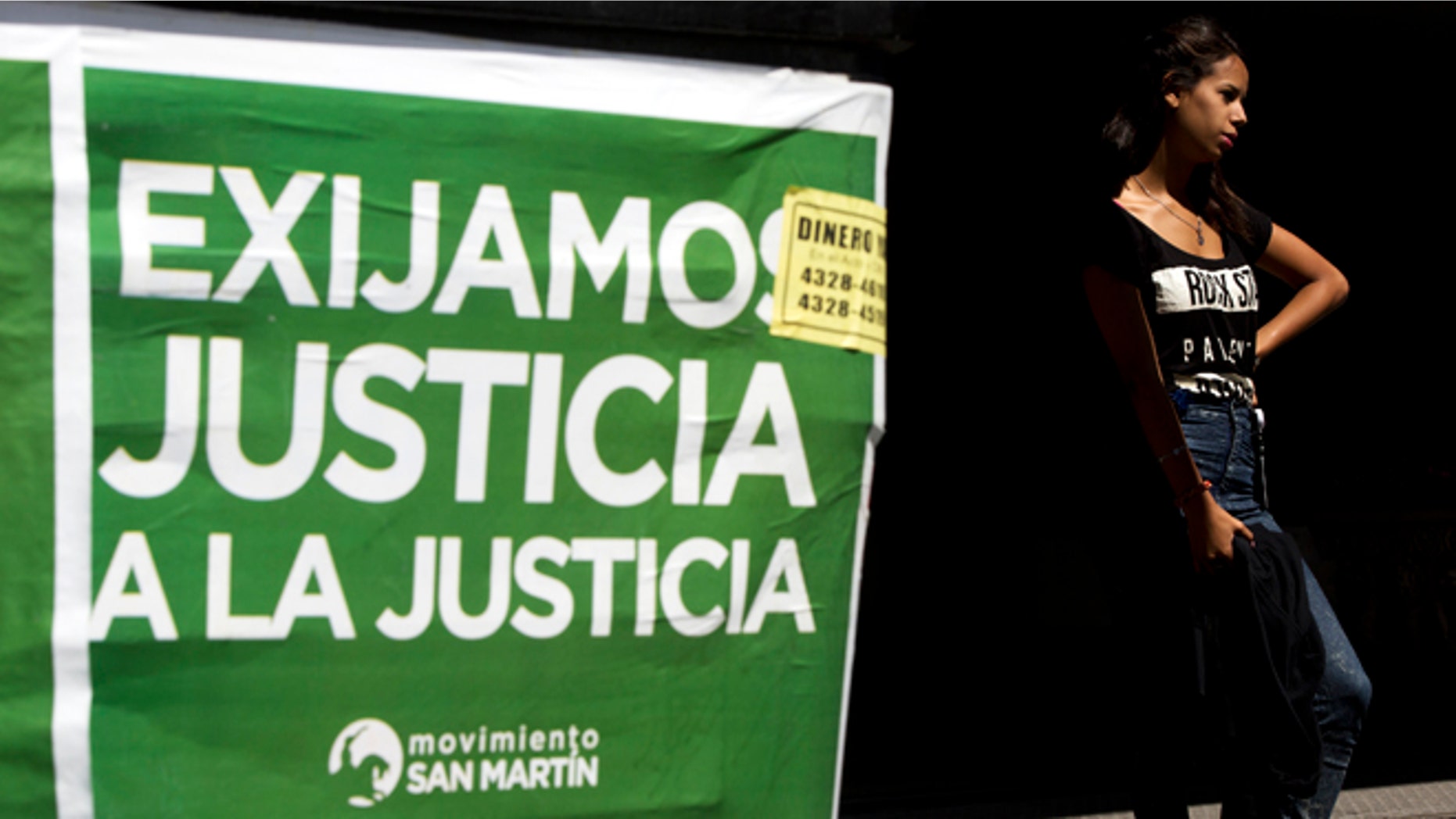 A woman stands next to a poster that reads in Spanish "Demand justice to justice", in reference to march organized by federal prosecutors demanding justice after the death of special prosecutor Alberto Nisman almost a month ago, in Buenos Aires, Argentina, Friday, Feb. 13, 2015. Nisman accused President Cristina Fernandez, Foreign Minister Hector Timerman and others in her administration of brokering the cover-up in the bombing of a Jewish community center in exchange for favorable deals on oil and other goods from Iran. Fernandez and Timerman have strongly denied the accusations, and Iran has repeatedly denied involvement in the bombing, which killed 85 people. (AP Photo/Rodrigo Abd)