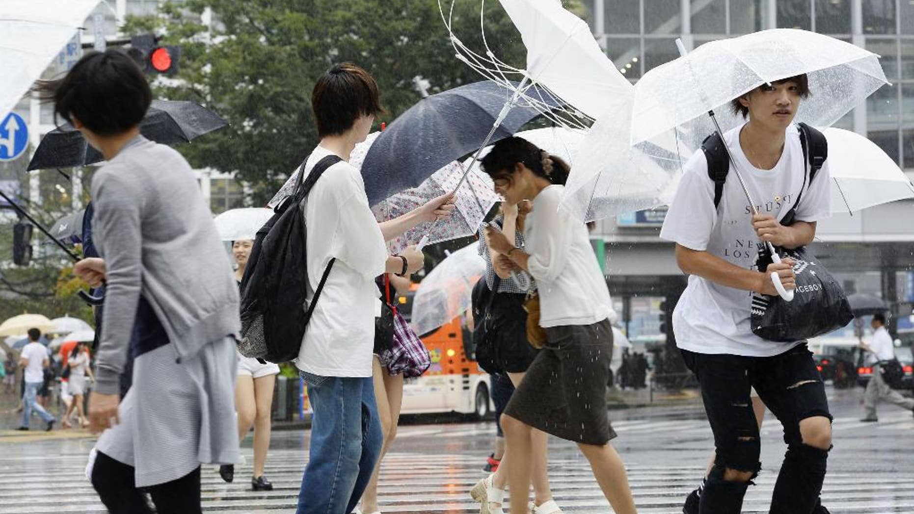 People walk in a strong wind caused by Typhoon Mindulle, in Tokyo Monday, Aug. 22, 2016. The typhoon sweeping through Tokyo and surrounding areas has forced the cancellation of more than 400 domestic flights in Japan and disrupted train service. (Akiko Matsushita/Kyodo News via AP)