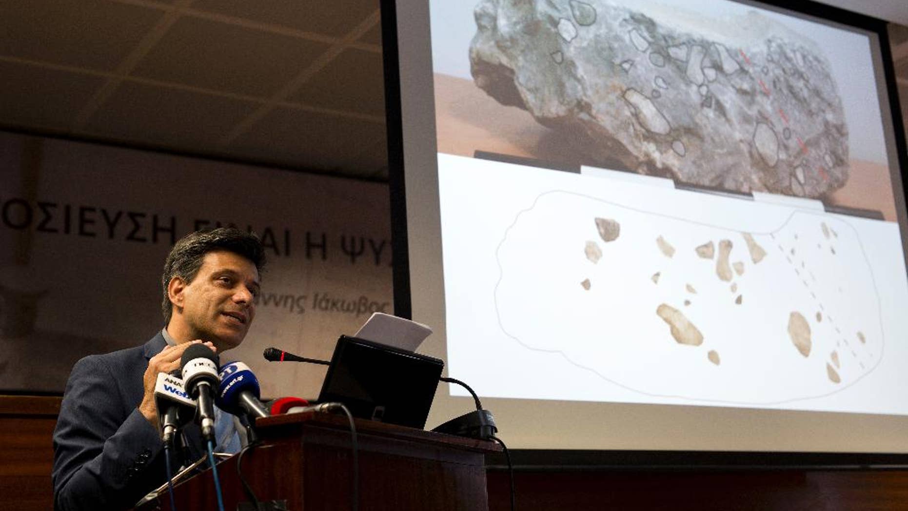 Greek archaeologist Christofilis Maggidis speaks as a photograph of a stone he believes belonged to the lost royal throne in the ancient palace of Mycenae, heart of the Mycenaean civilization, in southern Greece, during a press conference in Athens, on Tuesday, June 14, 2016. Maggidis says the worked stone, found by chance two years ago under the prehistoric citadel, is a chunk of the monolithic throne that was smashed when an earthquake sent part of the palace tumbling into a streambed below. (AP Photo/Petros Giannakouris