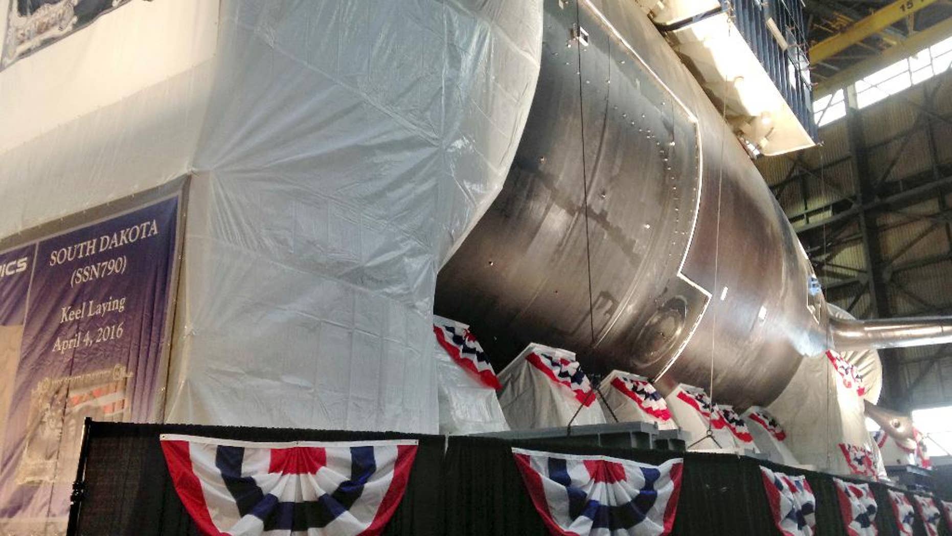 A module of the stern section of the nation's 17th Virginia-class attack submarine South Dakota is visible behind a backdrop during a ceremony at the manufacturing plant for General Dynamics' Electric Boat Monday, April 4, 2016, in North Kingstown, R.I. The keel of the nation's 17th Virginia-class attack submarine named for South Dakota is being laid at the manufacturing plant for General Dynamics' Electric Boat. The submarine doesn't have a traditional keel running the length of the ship, but is built in modules. (AP Photo/Jennifer McDermott)