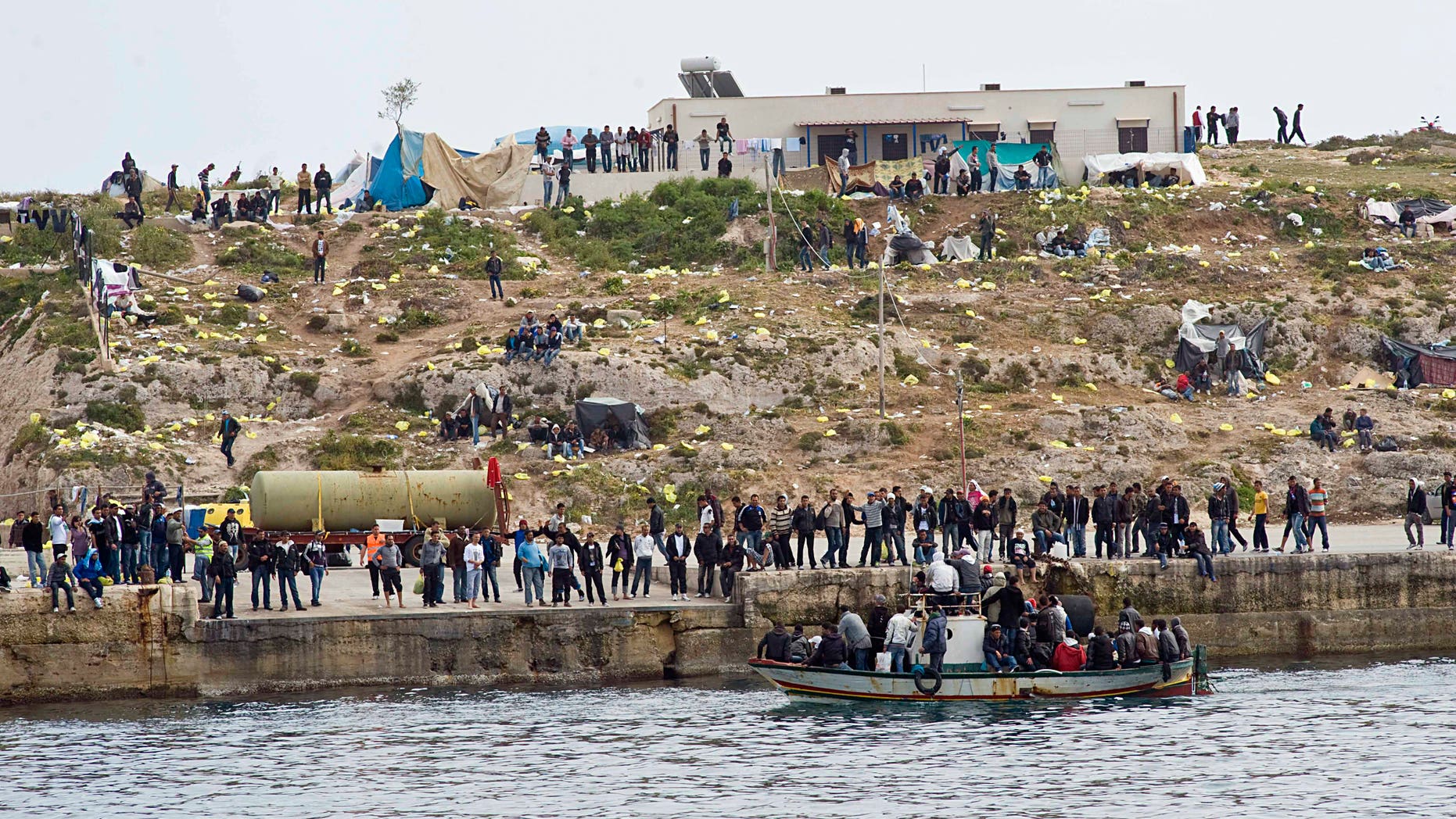 Migrants on a boat approach the Lampedusa harbor, Italy, Monday, March 28, 2011. Fishermen have used empty migrants' boats to block the entrance to Lampedusa harbor, a mostly symbolic act which still raised cheers from townsfolk gathered on the quays. News reports Monday said the boats, which had been seized by Italian authorities, were used to block the tiny island's port. Officials reported 460 migrants arrived from North Africa overnight, joining 3,000 more who have arrived in the last three days and escalating tensions on the island, closer to Africa than to mainland Italy.